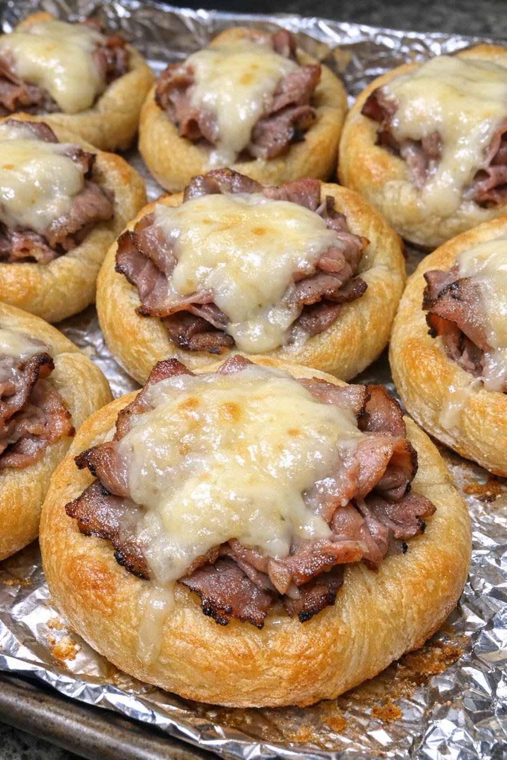 Golden brown crescent dough nests filled with roast beef and taleggio cheese on a baking sheet