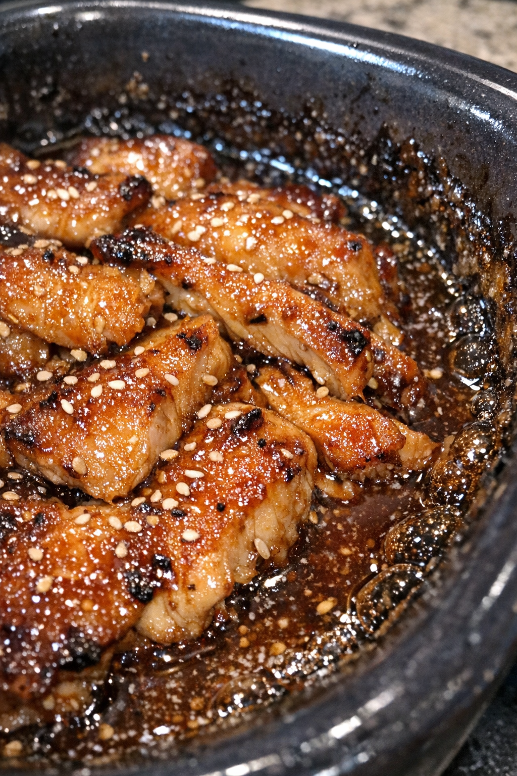 Glistening roasted chicken in a dark ceramic baking dish