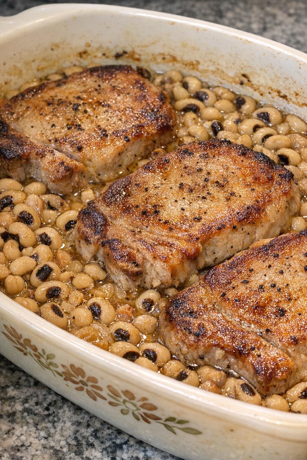 Golden browned pork chops baked over black-eyed peas in a vintage casserole dish