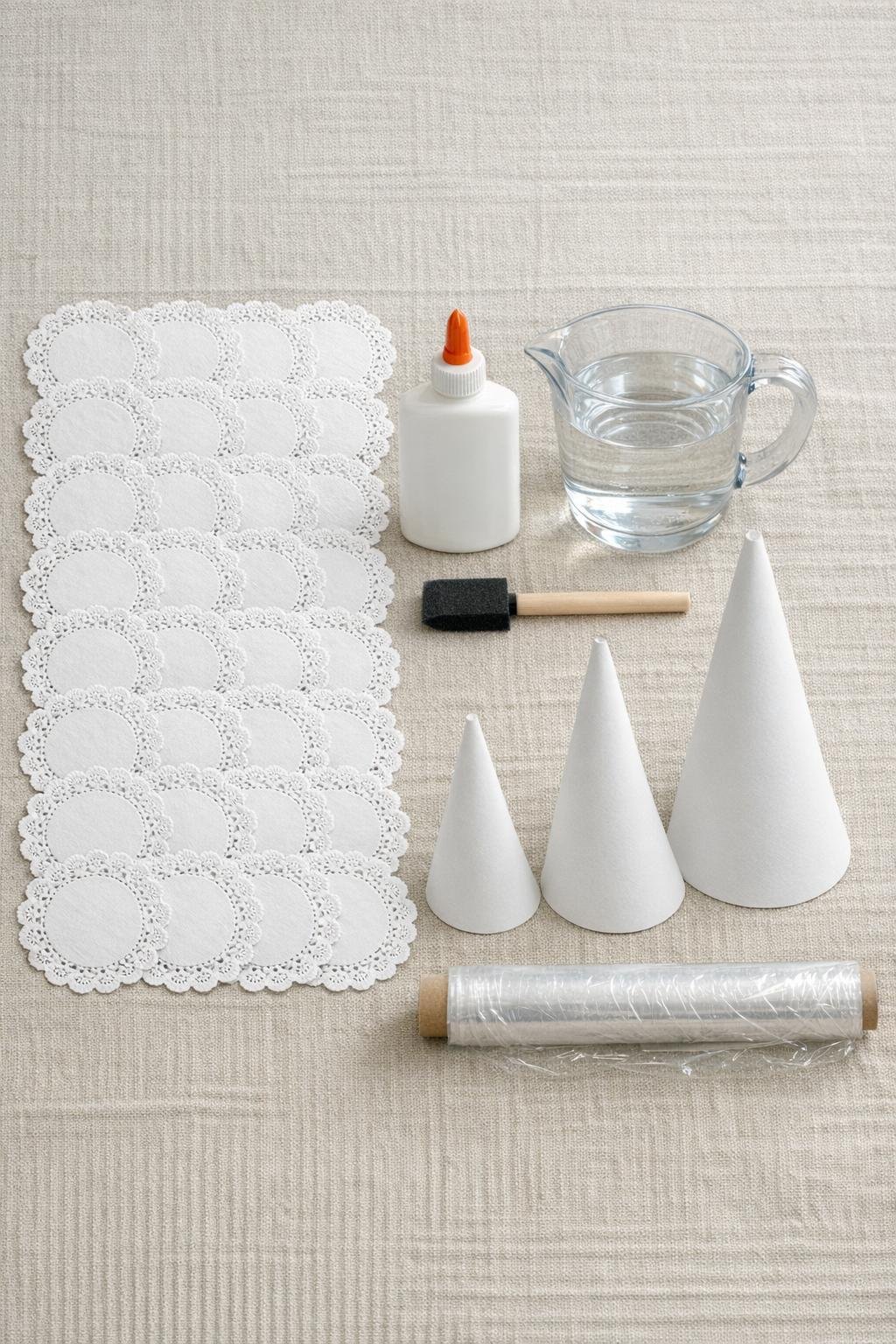 Paper doilies, glue, water, foam brush, poster board cones, and plastic wrap laid out together