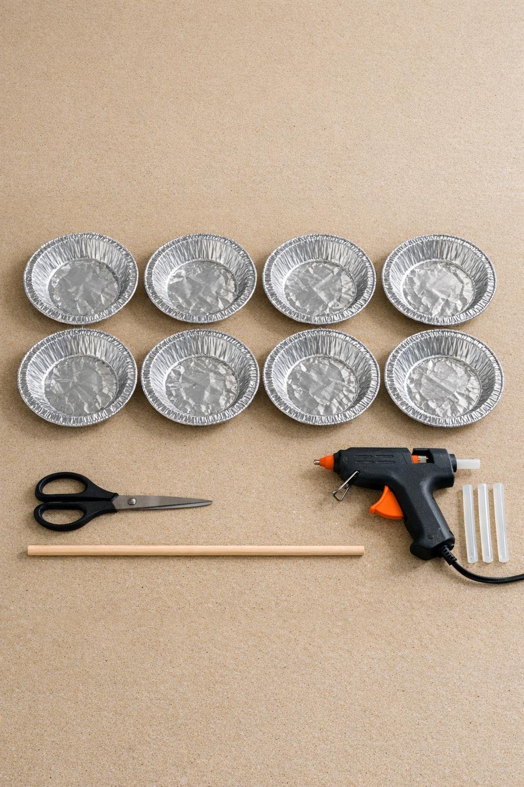 Foil pie tins, scissors, dowel, and glue gun laid out on a craft table
