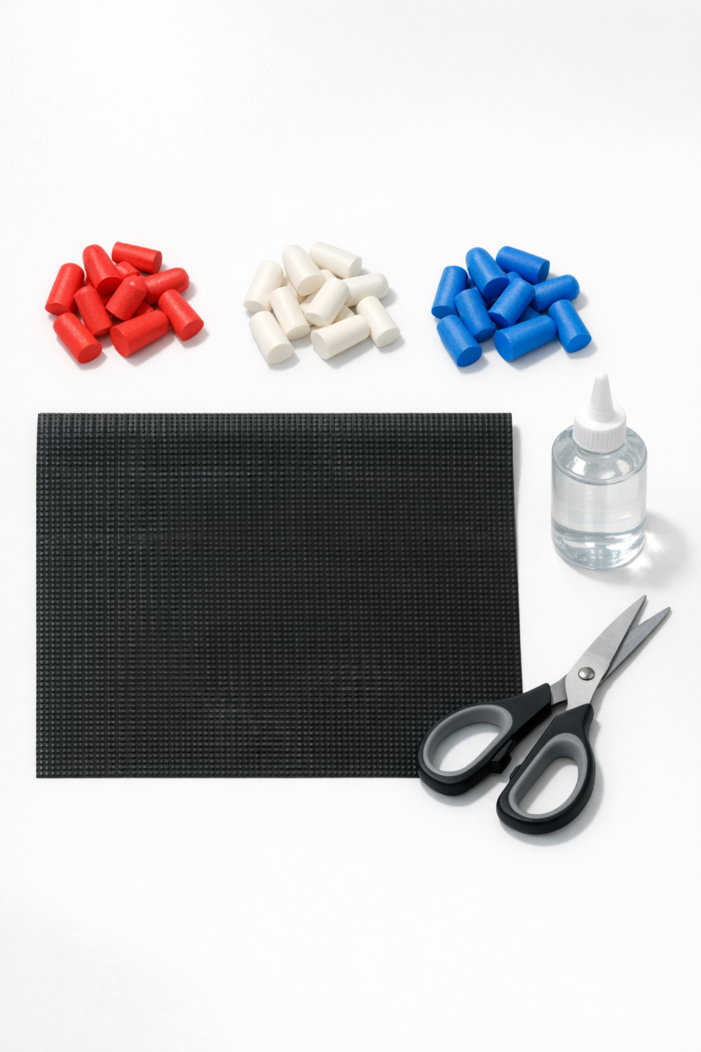 Red, white, and blue foam earplugs with shelf liner, craft glue, and scissors laid out for the project
