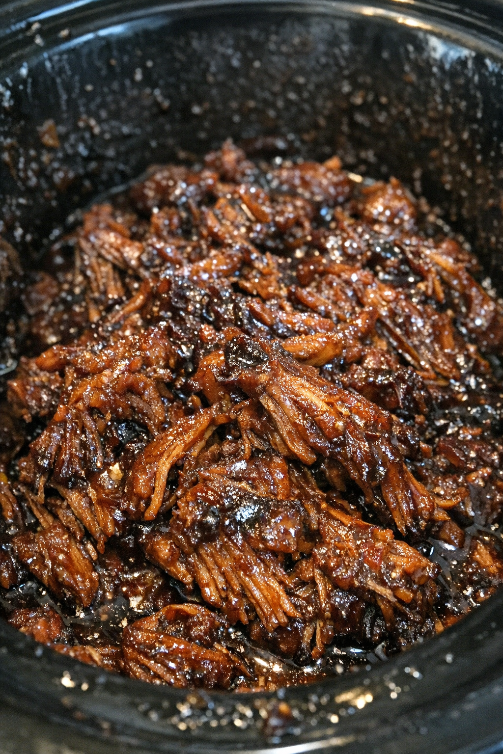 Slow-roasted shredded protein glazed in dark sauce in a slow cooker