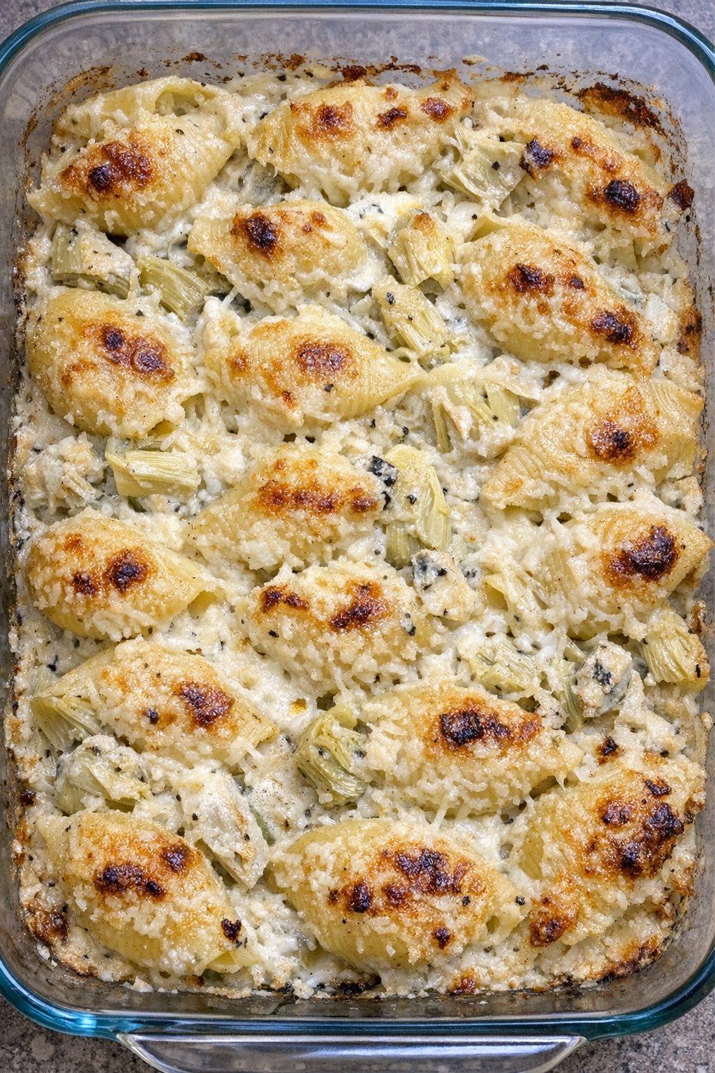 Golden baked artichoke parmesan shells in a glass baking dish