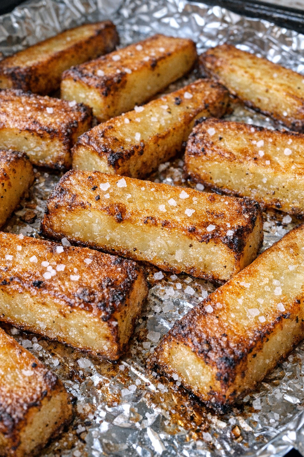 Thick-cut golden potato planks on a foil-lined baking sheet