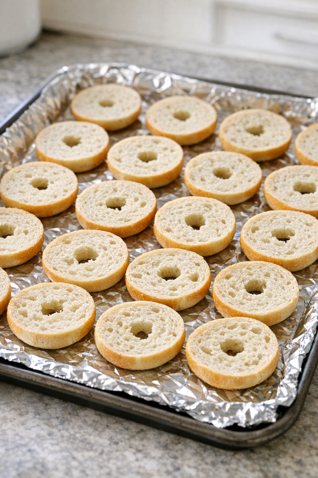Mini bagel halves arranged on a foil-lined baking sheet