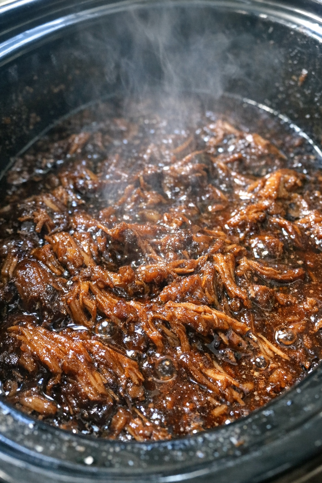 Slow cooker pulled pork bubbling in dark sauce