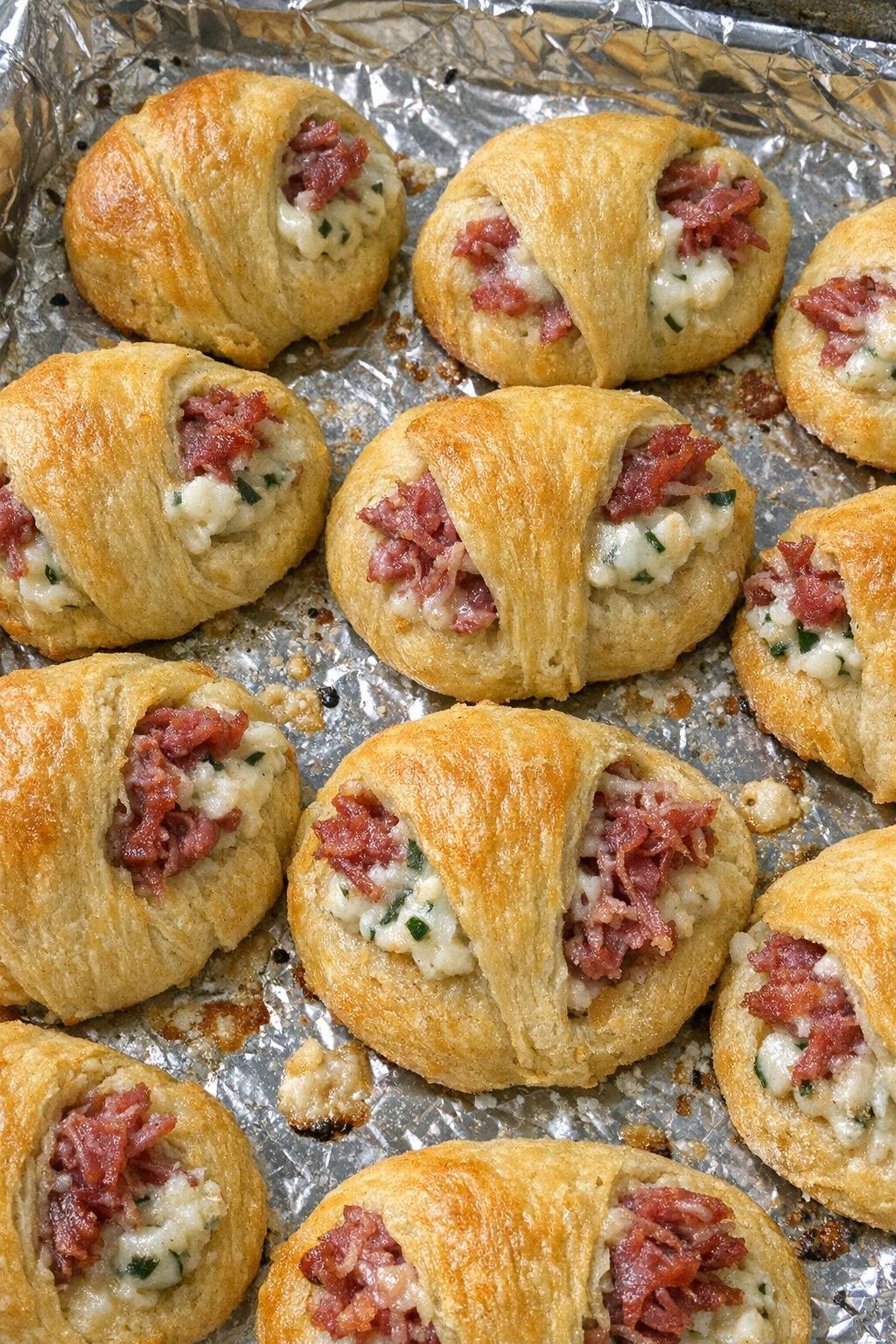 Flaky golden crescent rounds stuffed with shredded corned beef and creamy onion chive filling on a foil-lined baking sheet