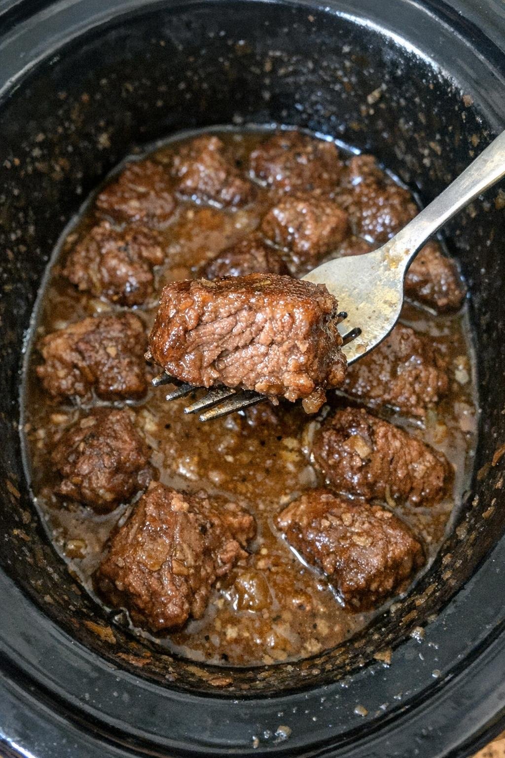 Tender beef stew meat in brown gravy in a slow cooker