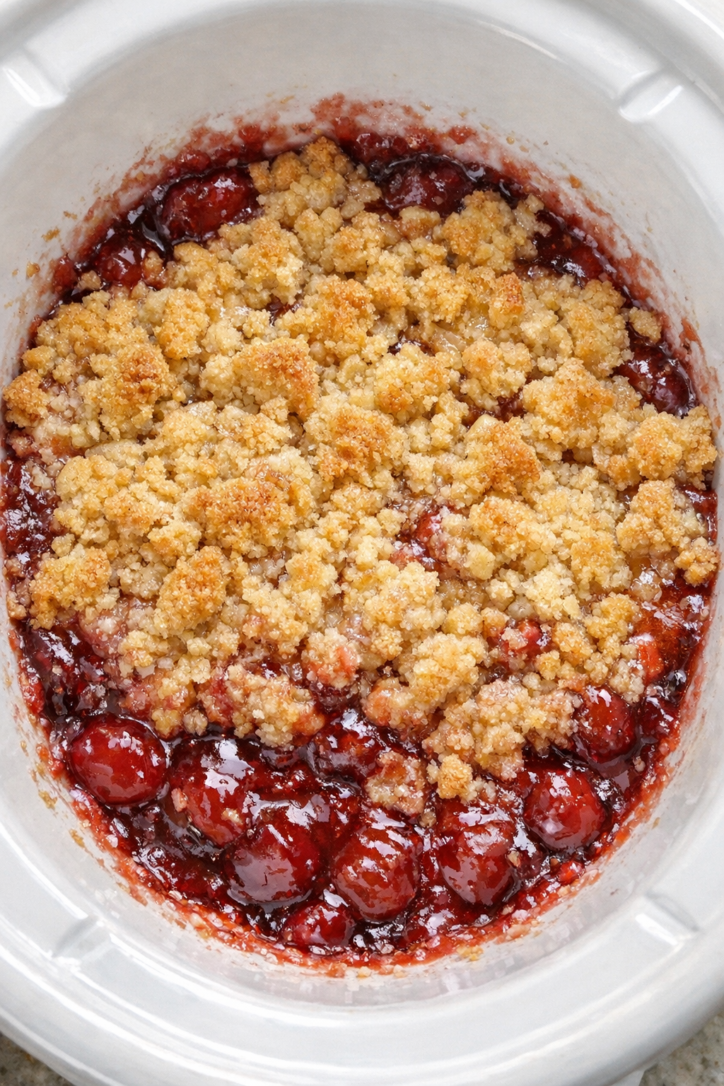 Slow cooker cherry dump cake with golden crumble in a white slow cooker