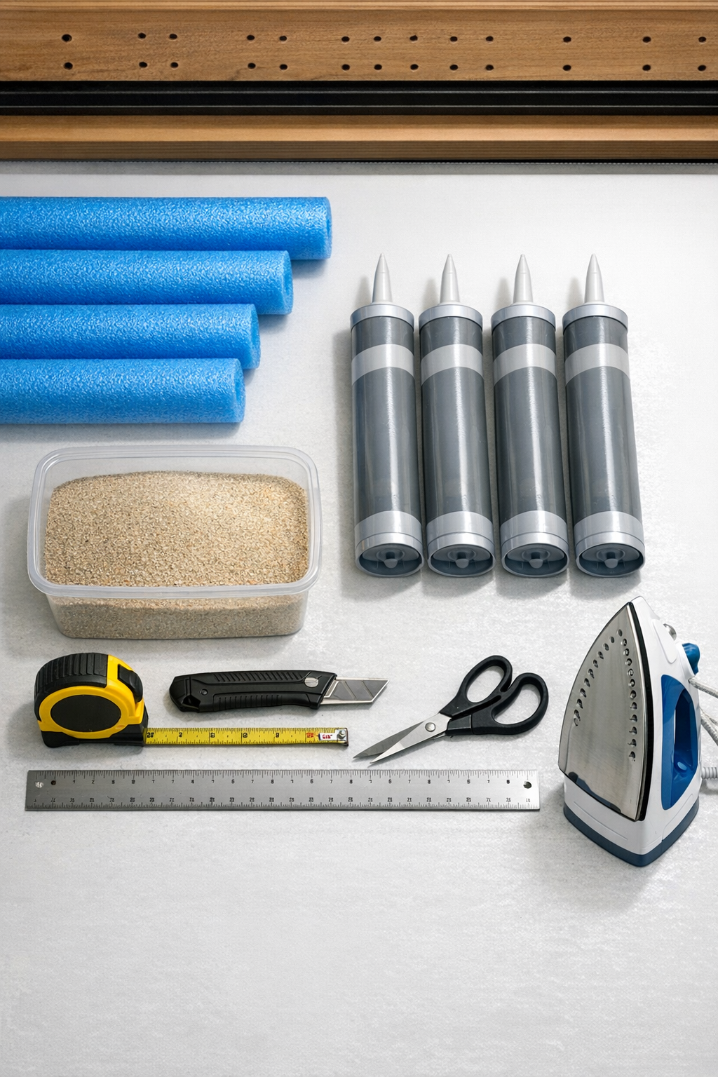 Pool noodles, acrylic caulk, and sand laid out with tools for driveway joint filler project