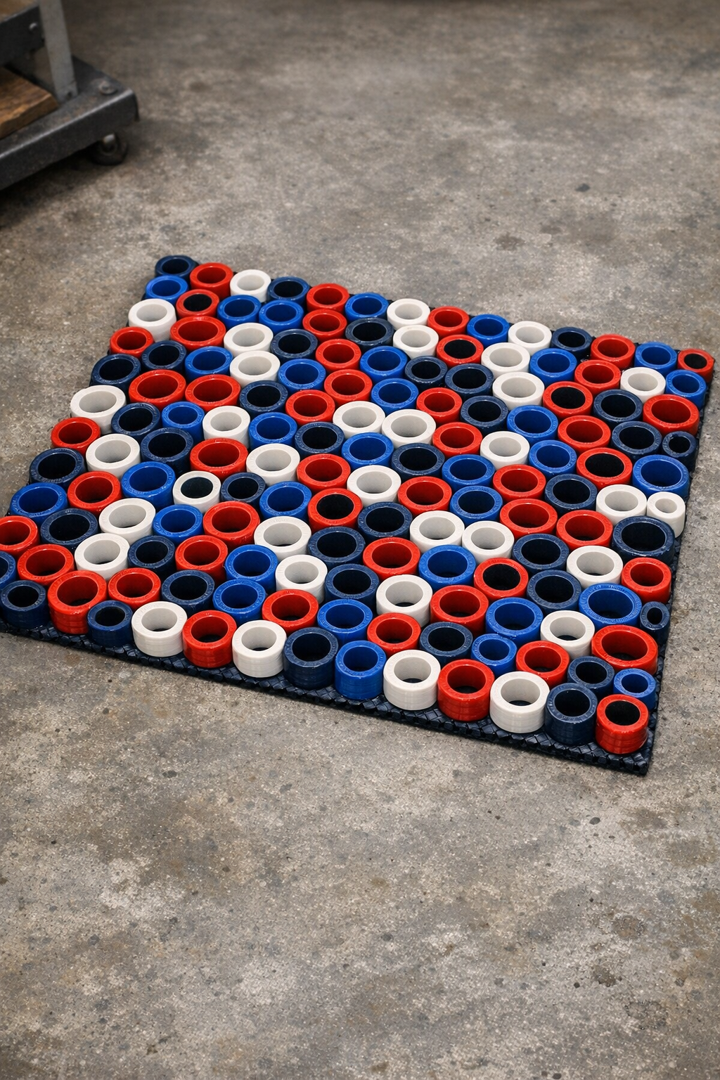 Finished red, white, and blue heavy-duty shop mat made from fused garden hose slices