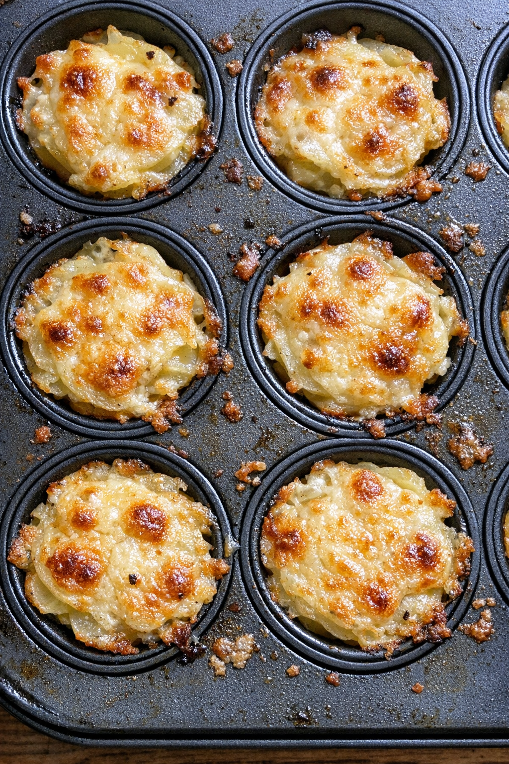 Individual golden bubbly potato gratin cups in a muffin tin