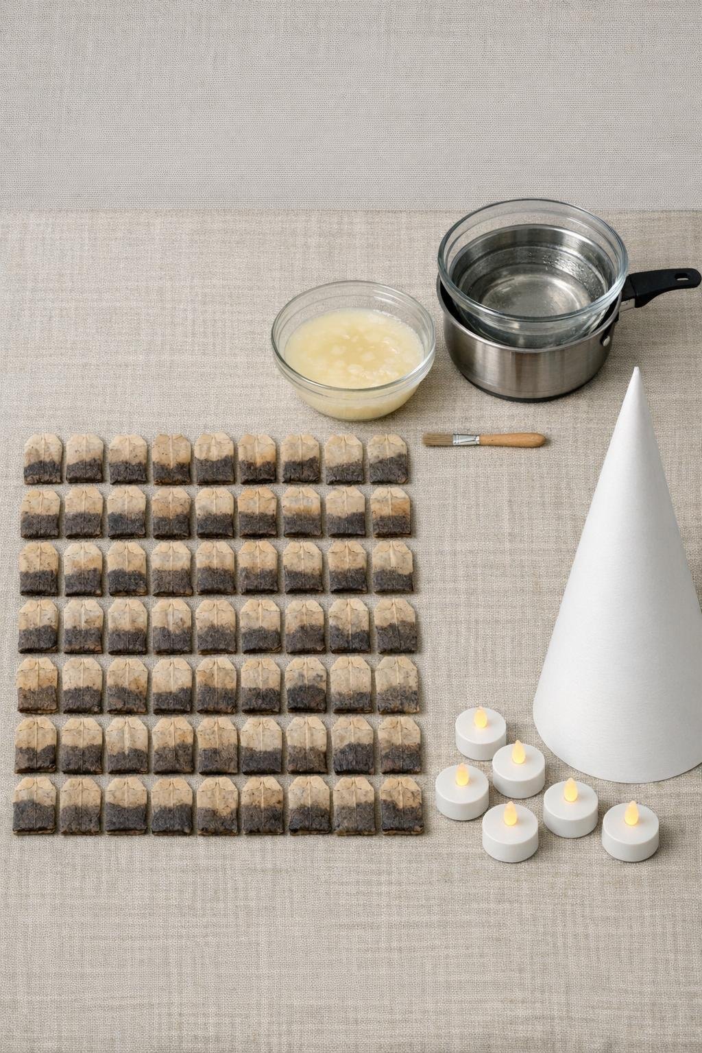 Used tea bags, candle wax, paintbrush, double boiler, poster board cone, and LED tea lights laid out together