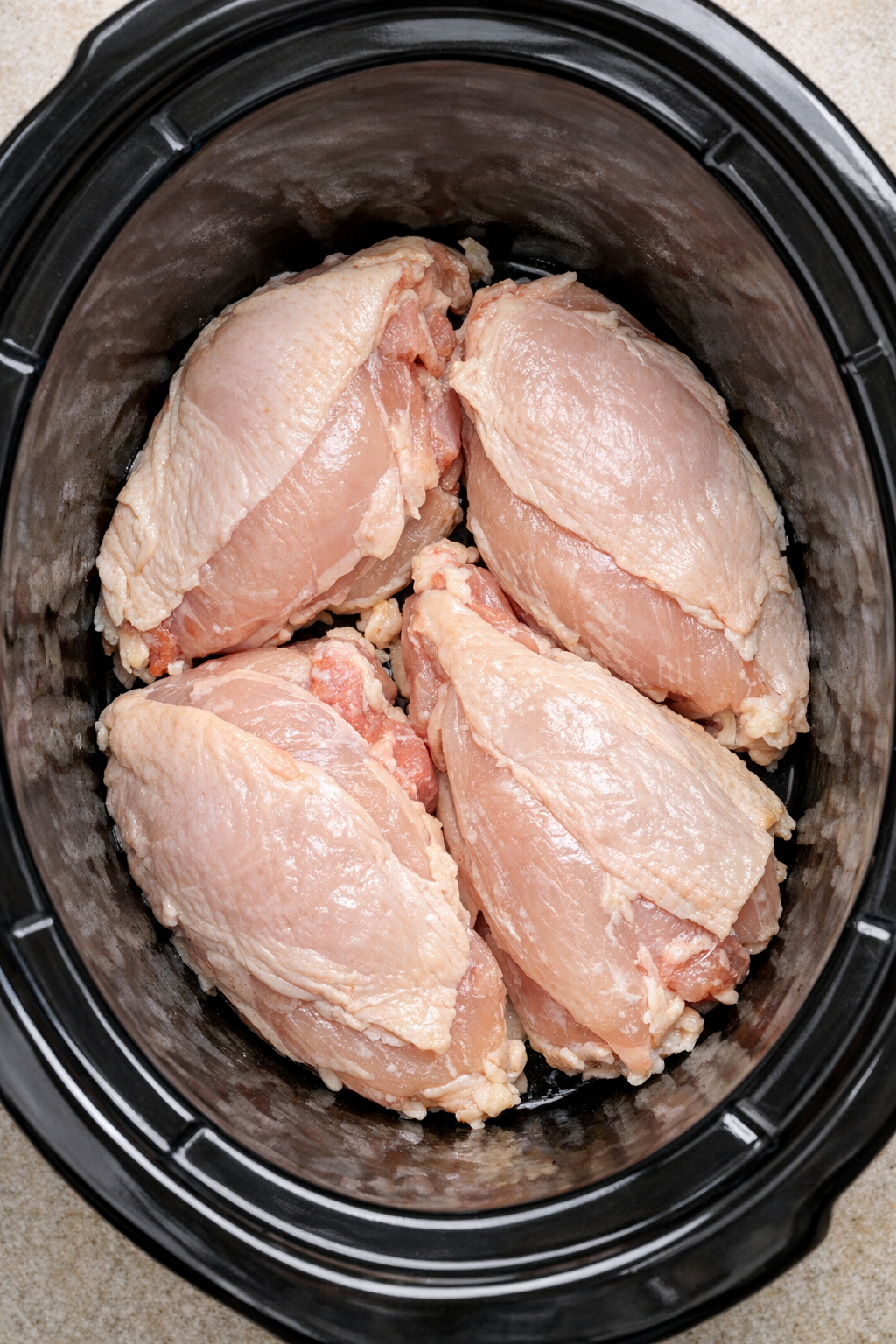 Raw split chicken breasts arranged in slow cooker
