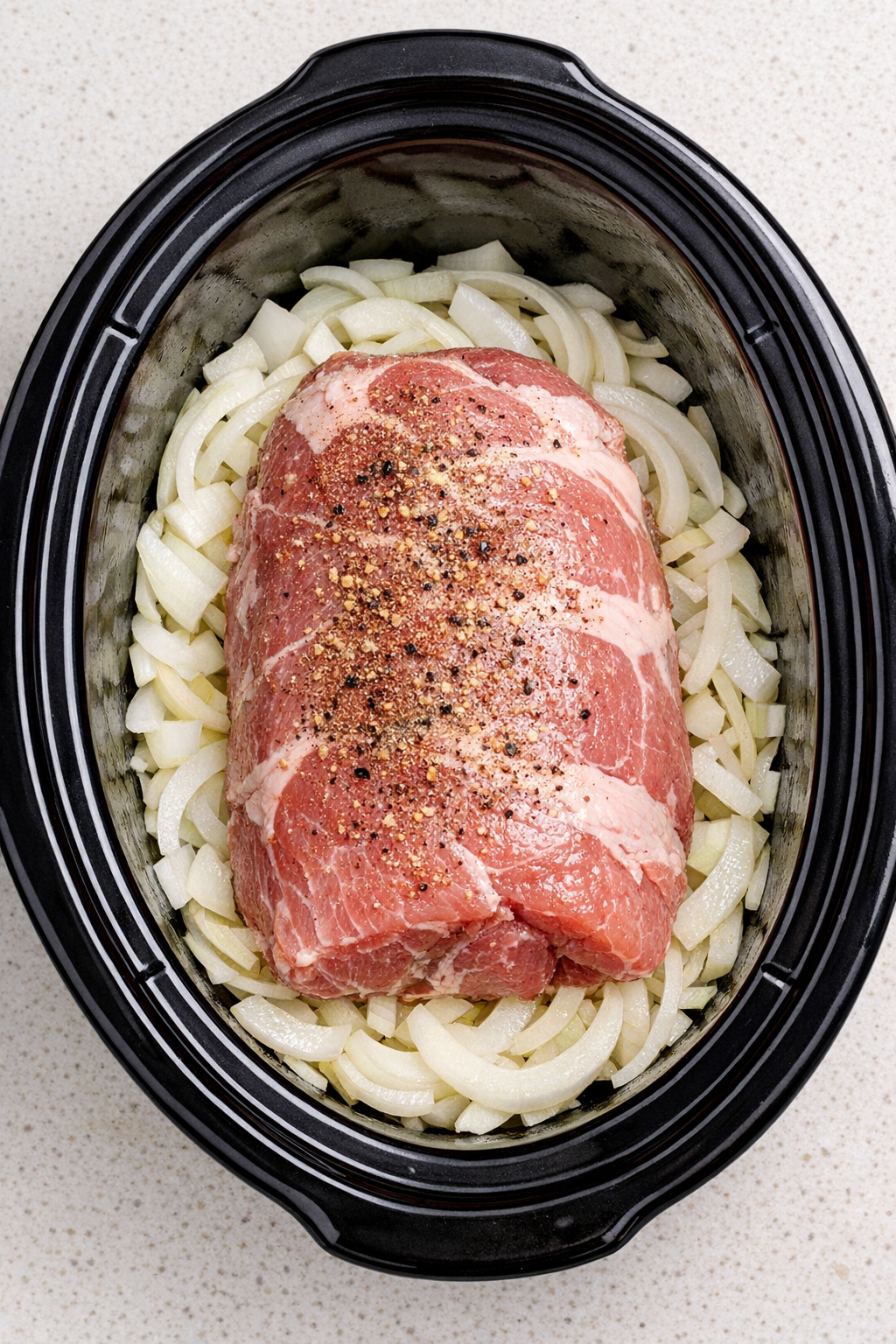 Onions and raw pork roast arranged in the slow cooker
