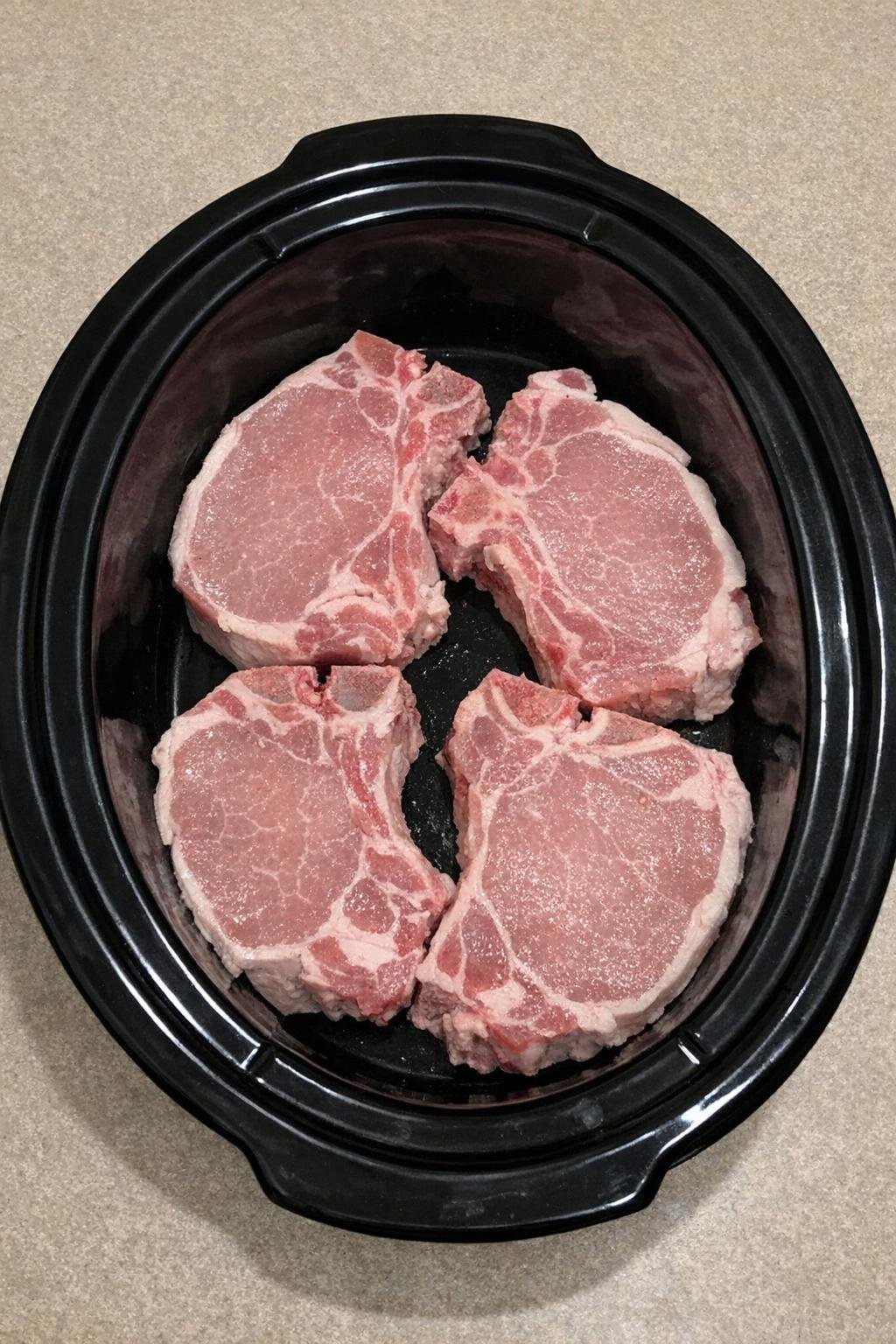 Raw bone-in pork chops in a slow cooker crock