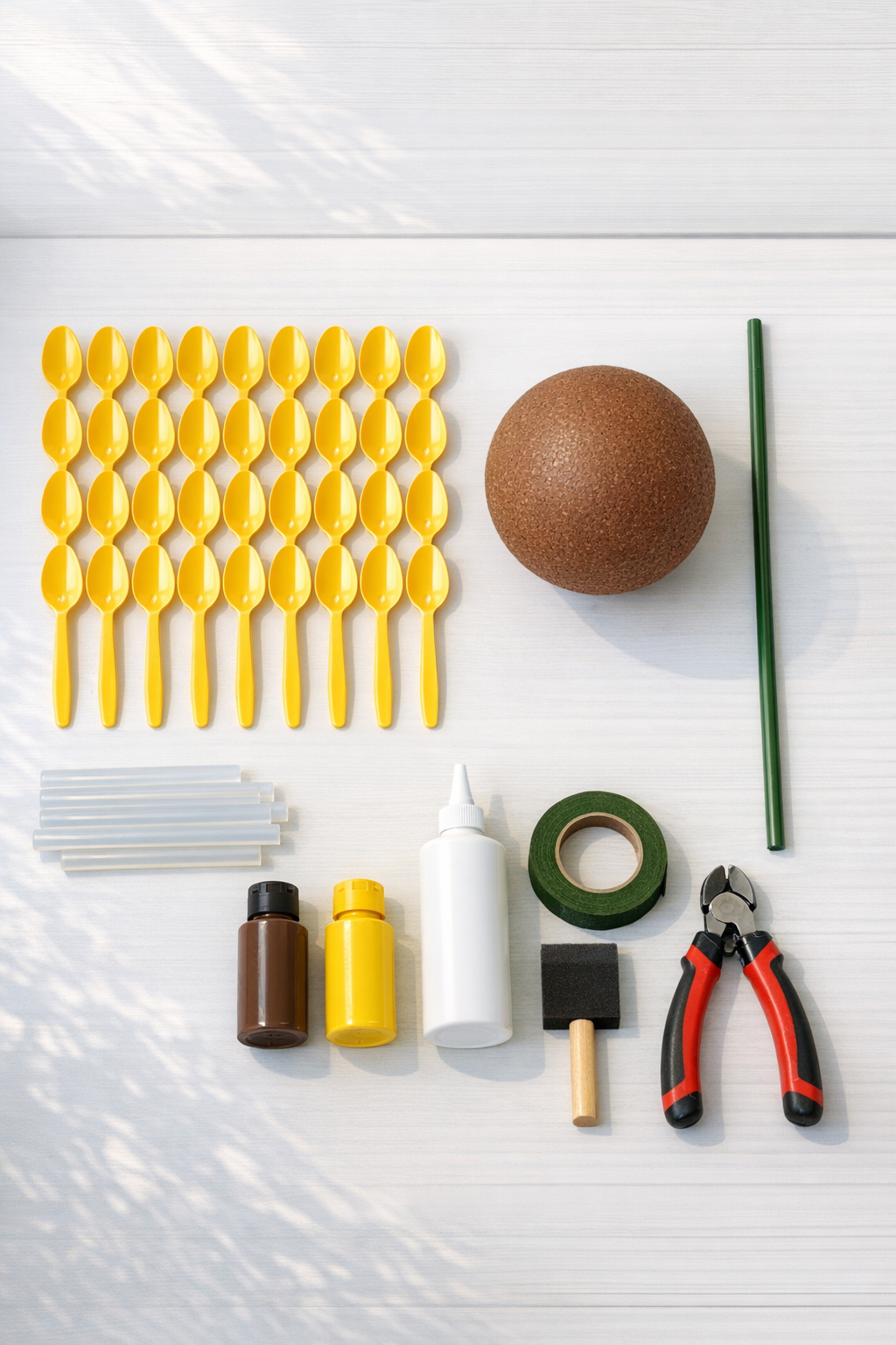 Yellow plastic spoons, a brown Styrofoam ball, green garden stake, glue, and paint supplies laid out on a table