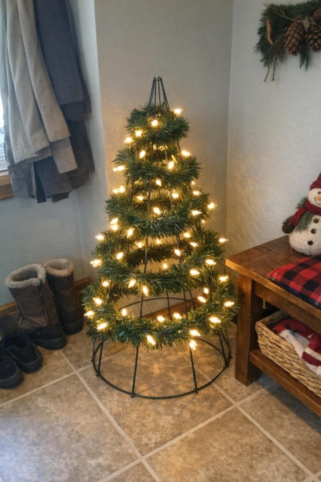 A tomato cage shaped into a small Christmas tree wrapped in lights and garland