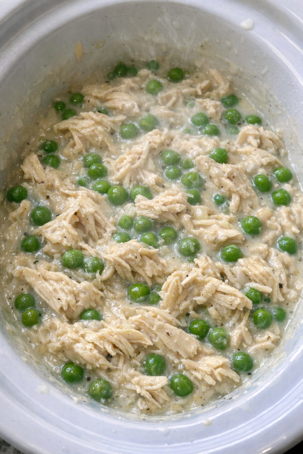 Slow cooker Amish chicken and peas in a white slow cooker