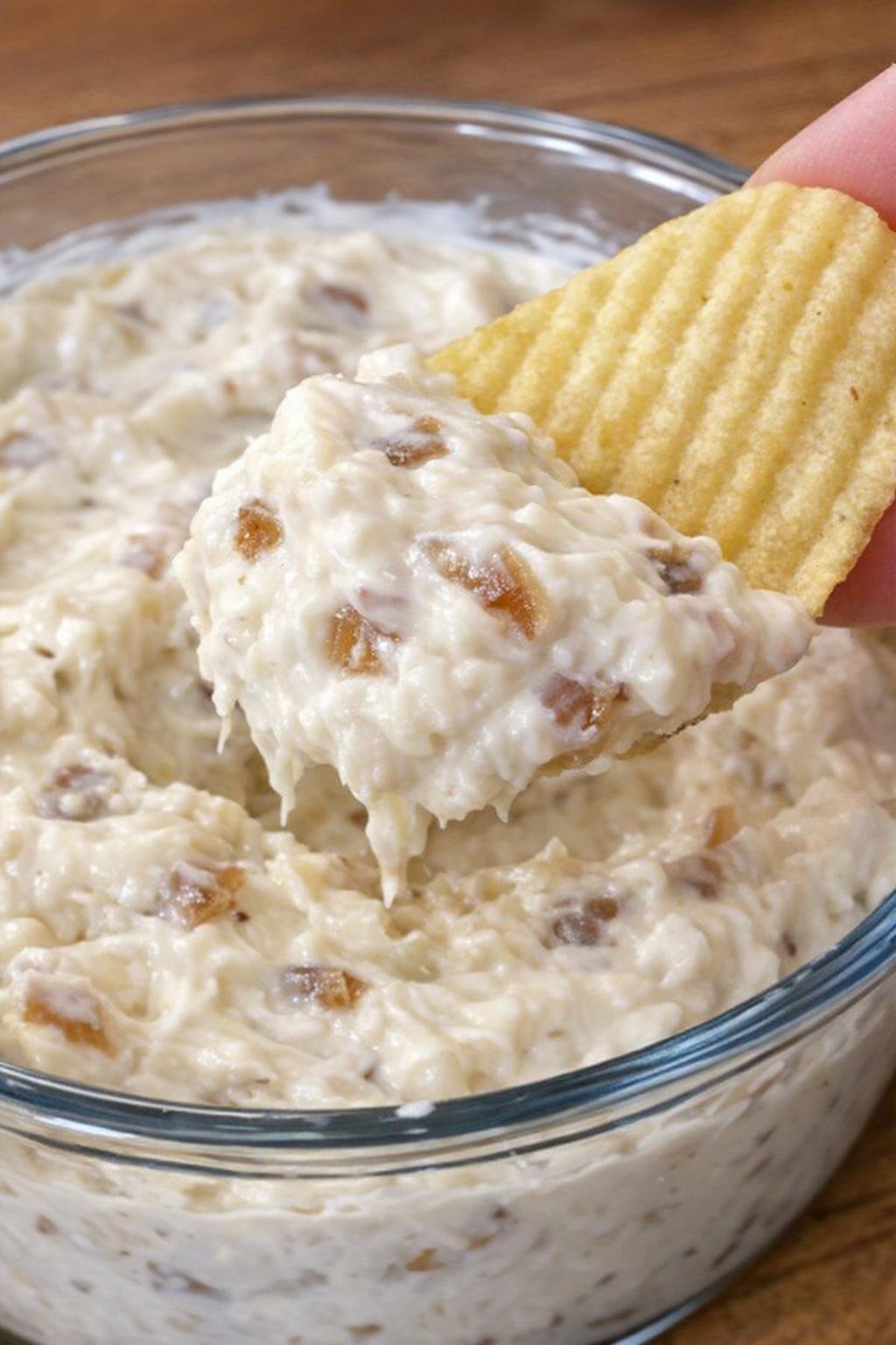 Onion barclay dip in a glass bowl with a potato chip scooping it