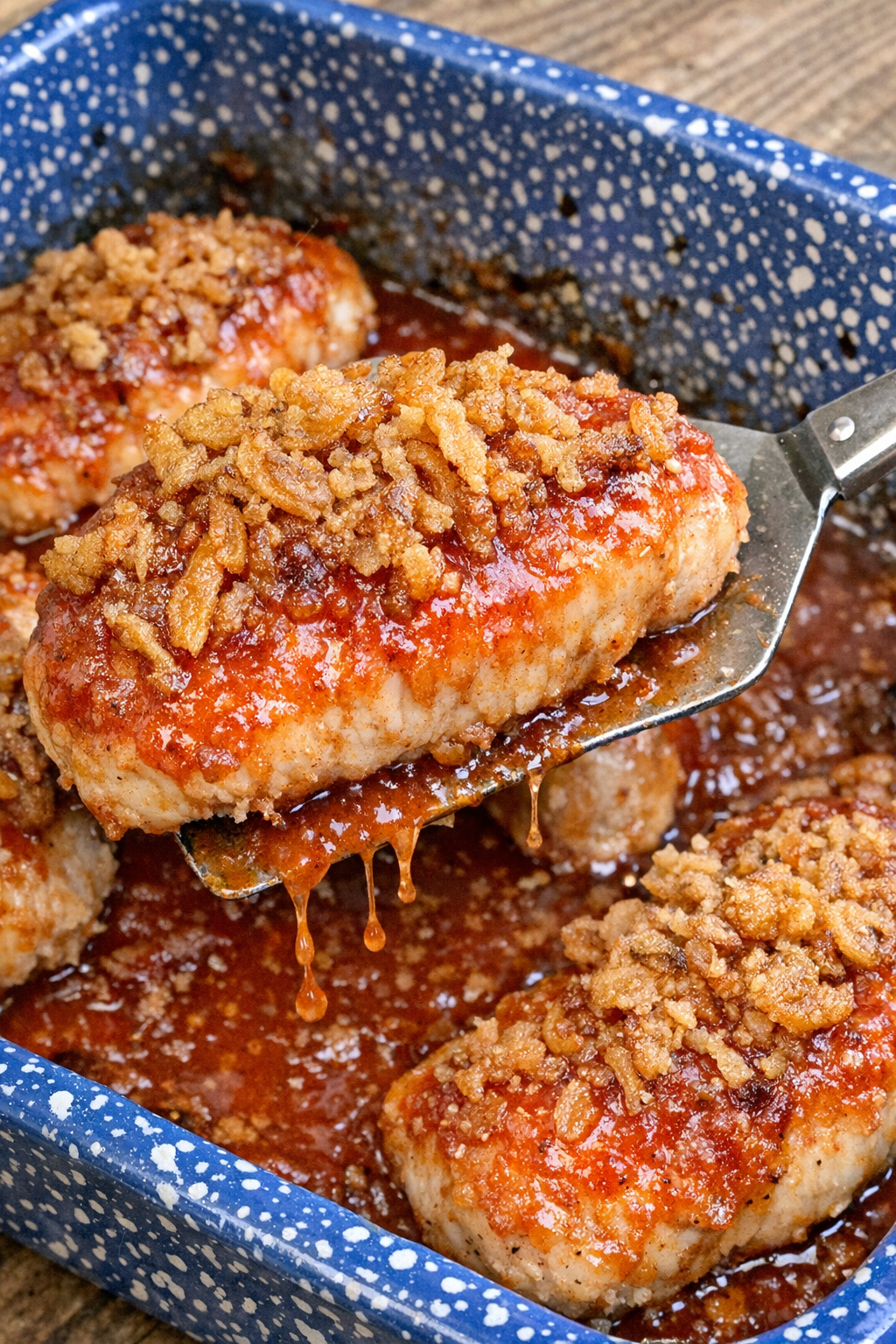 Crispy topped chicken breast pieces in tangy red dressing in a blue speckled baking dish