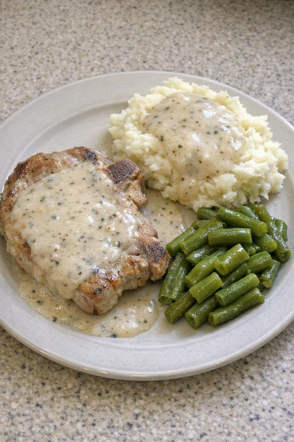 Family-style plate with pork chop, gravy, potatoes, and green beans