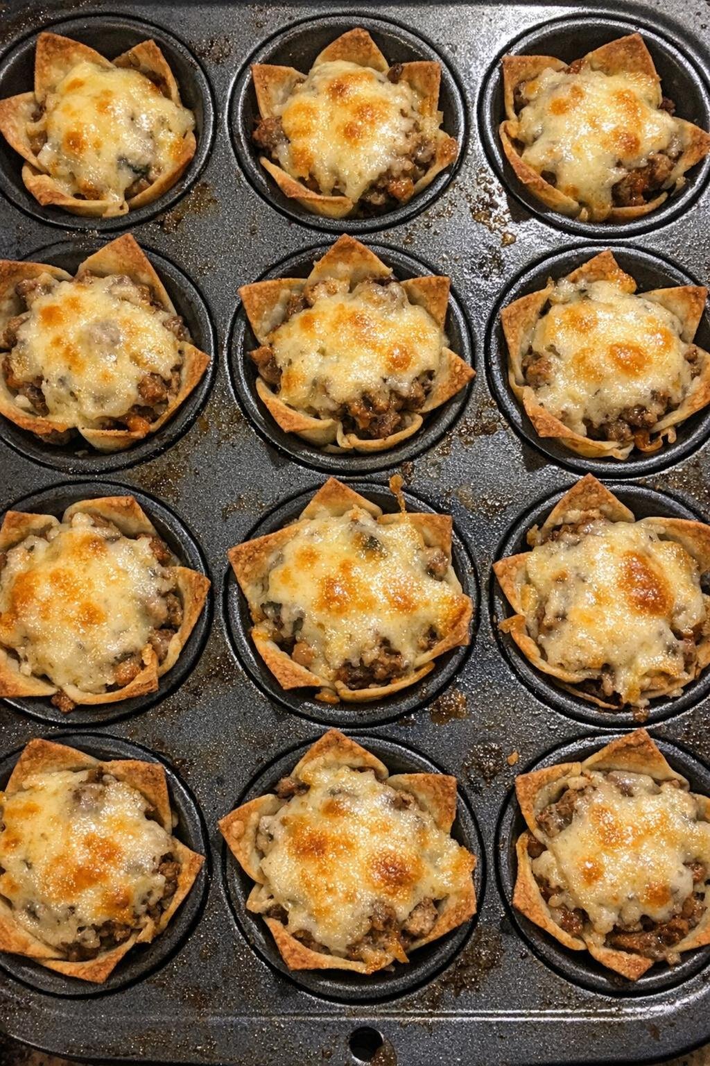 Crunchy party cups topped with melted cheese and savory filling in a muffin tin