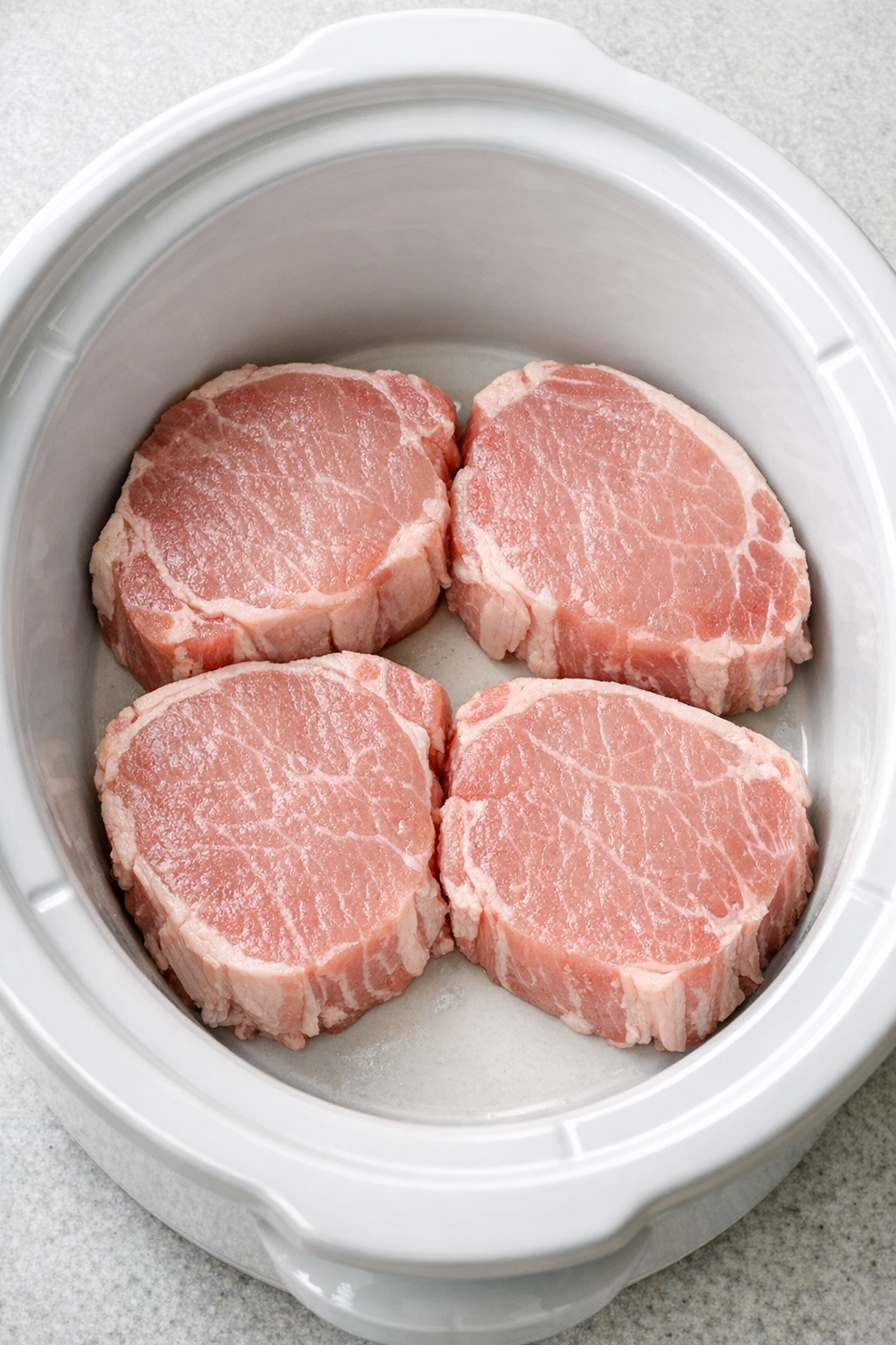 Raw pork chops arranged in the slow cooker