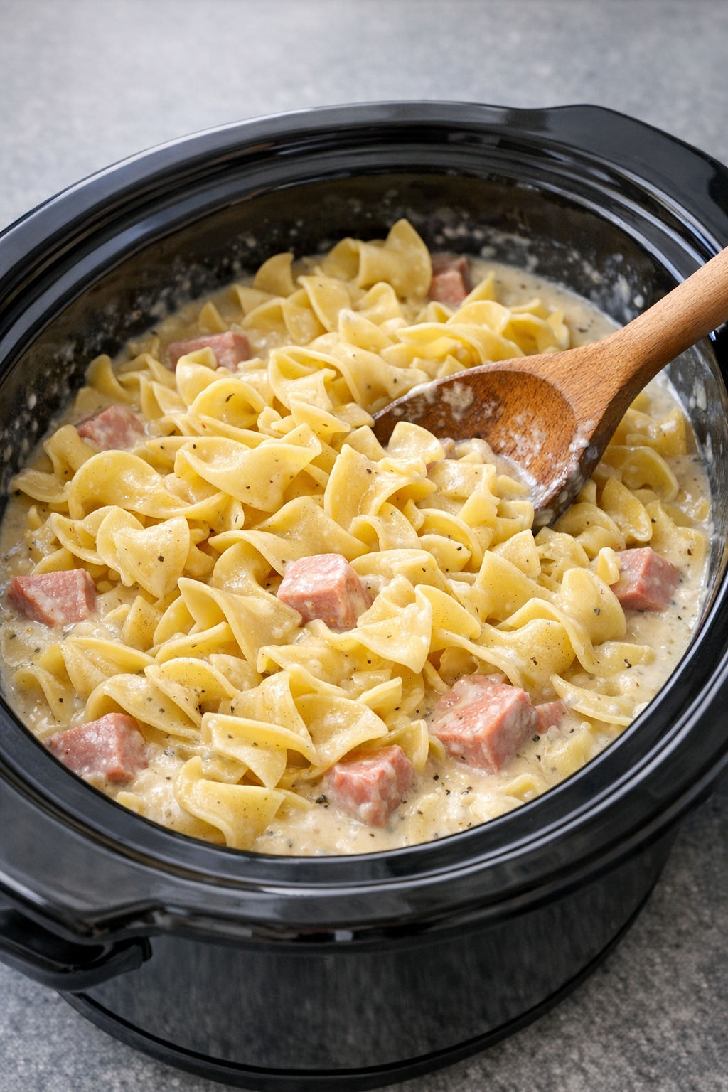 Egg noodles being stirred into the creamy ham mixture