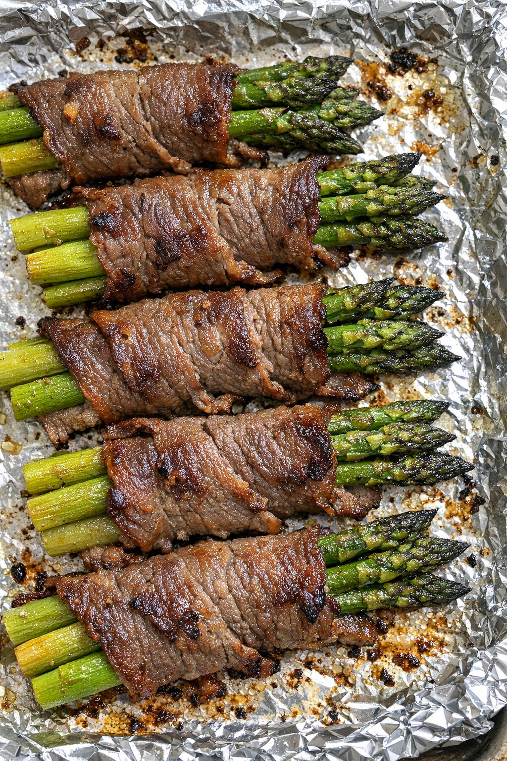 Oven baked beef wrapped asparagus on a foil-lined baking sheet