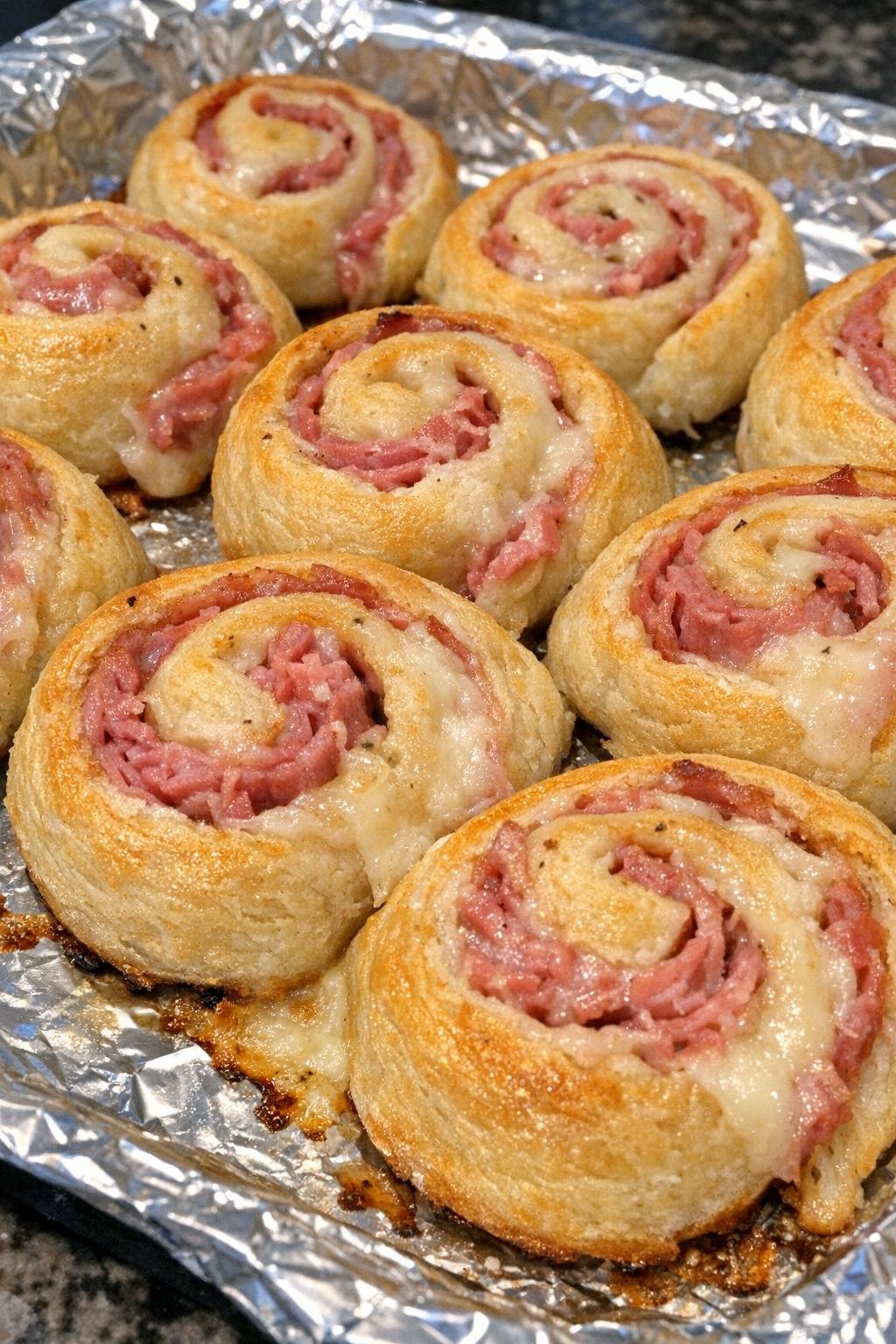 Golden crescent pinwheels with corned beef and fontina on a foil-lined baking sheet