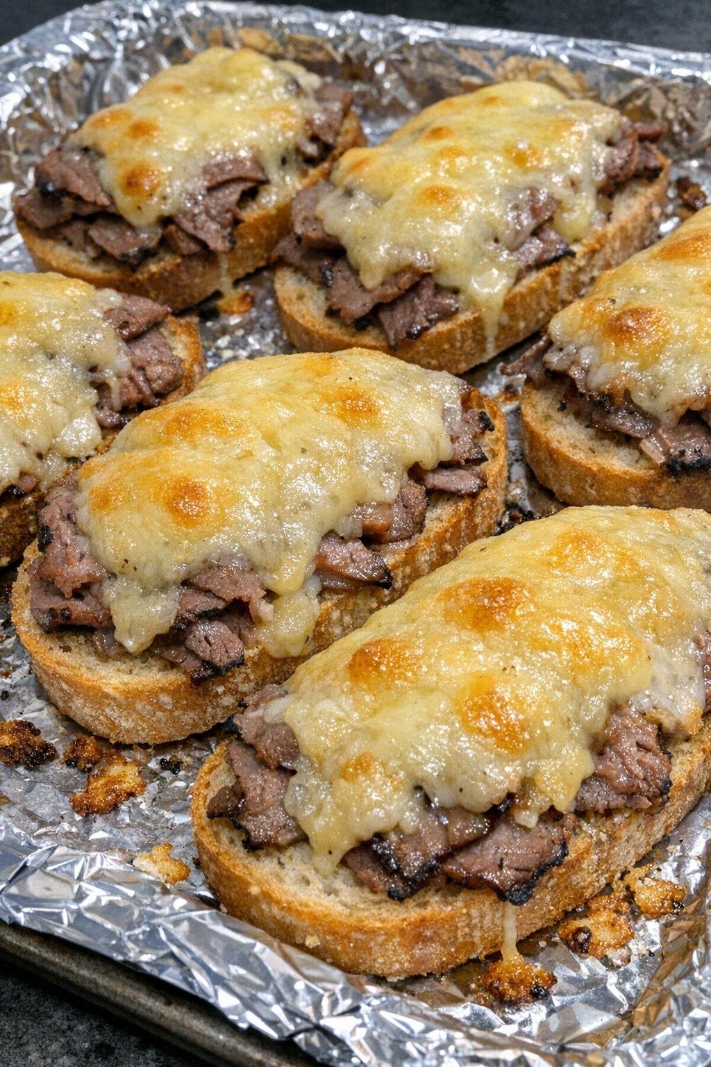 Oven baked beef and gouda crostini on a foil-lined baking sheet