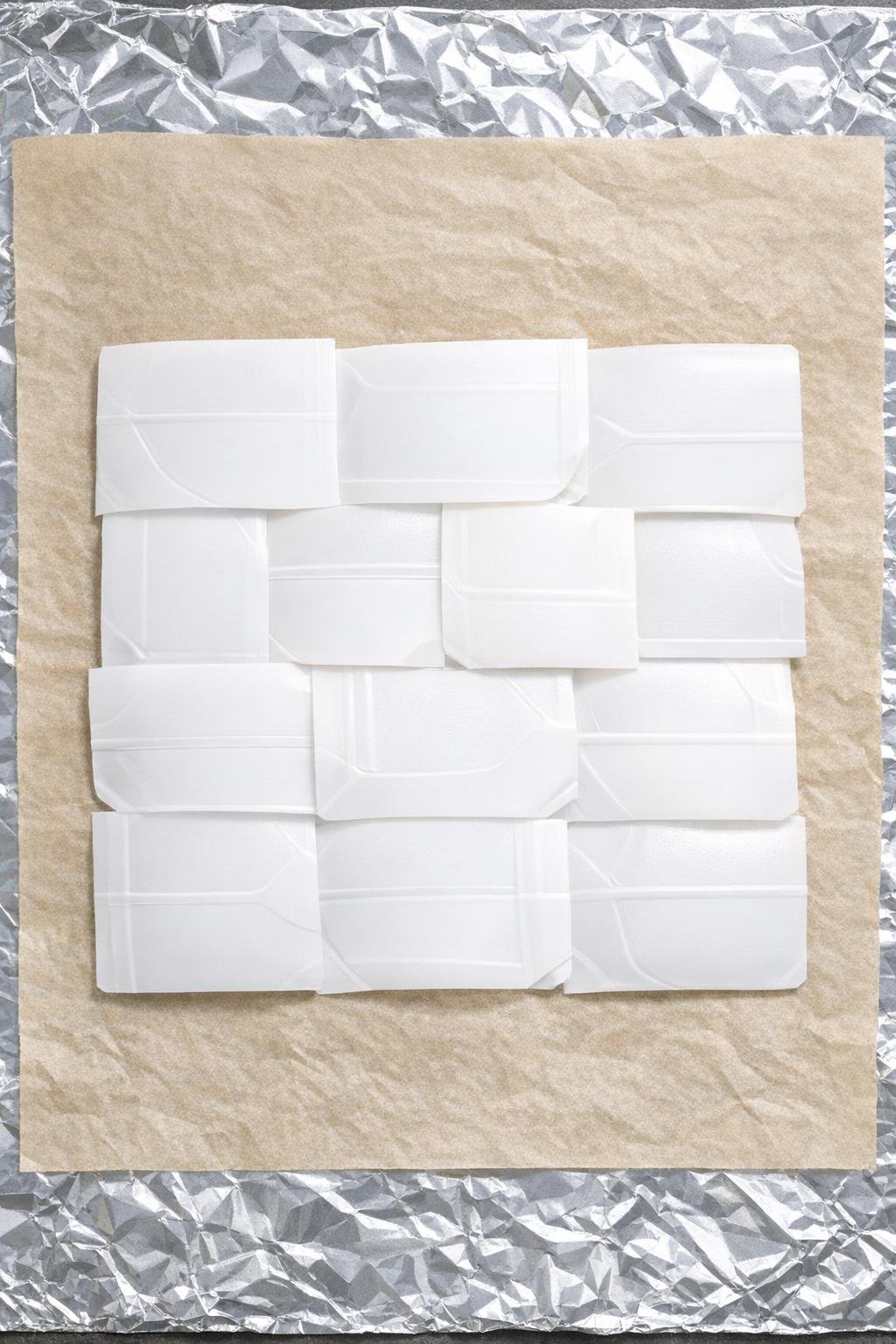 Layered white plastic panels arranged in overlapping rows on parchment and foil