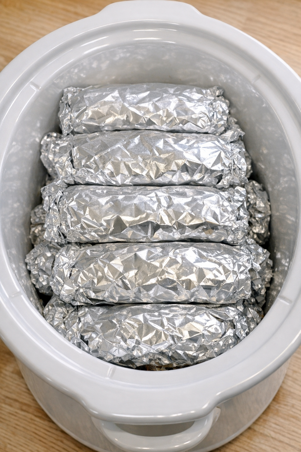 Foil packets stacked in a white slow cooker before serving