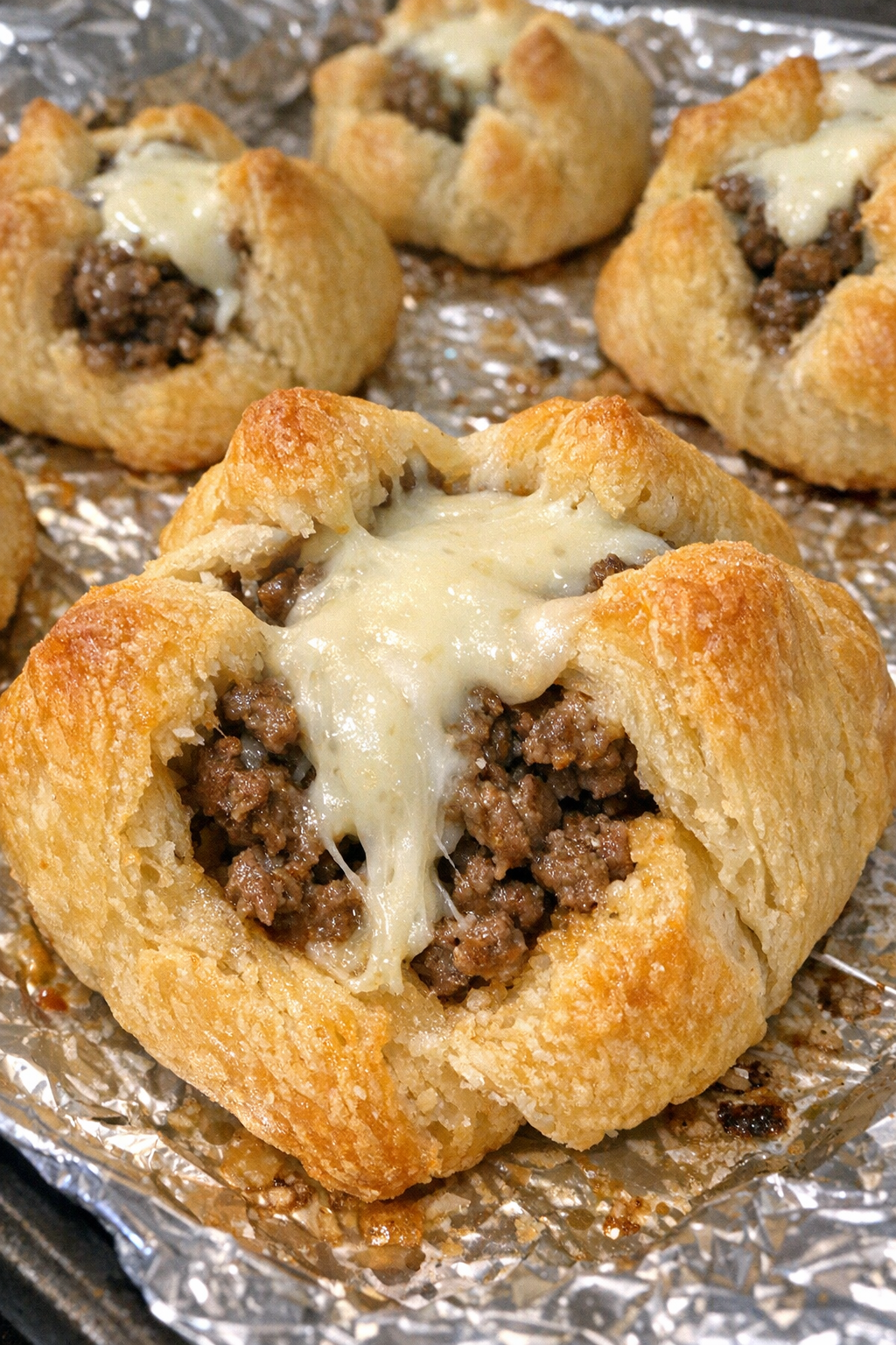Oven baked beef crescent blossoms on a foil-lined baking sheet