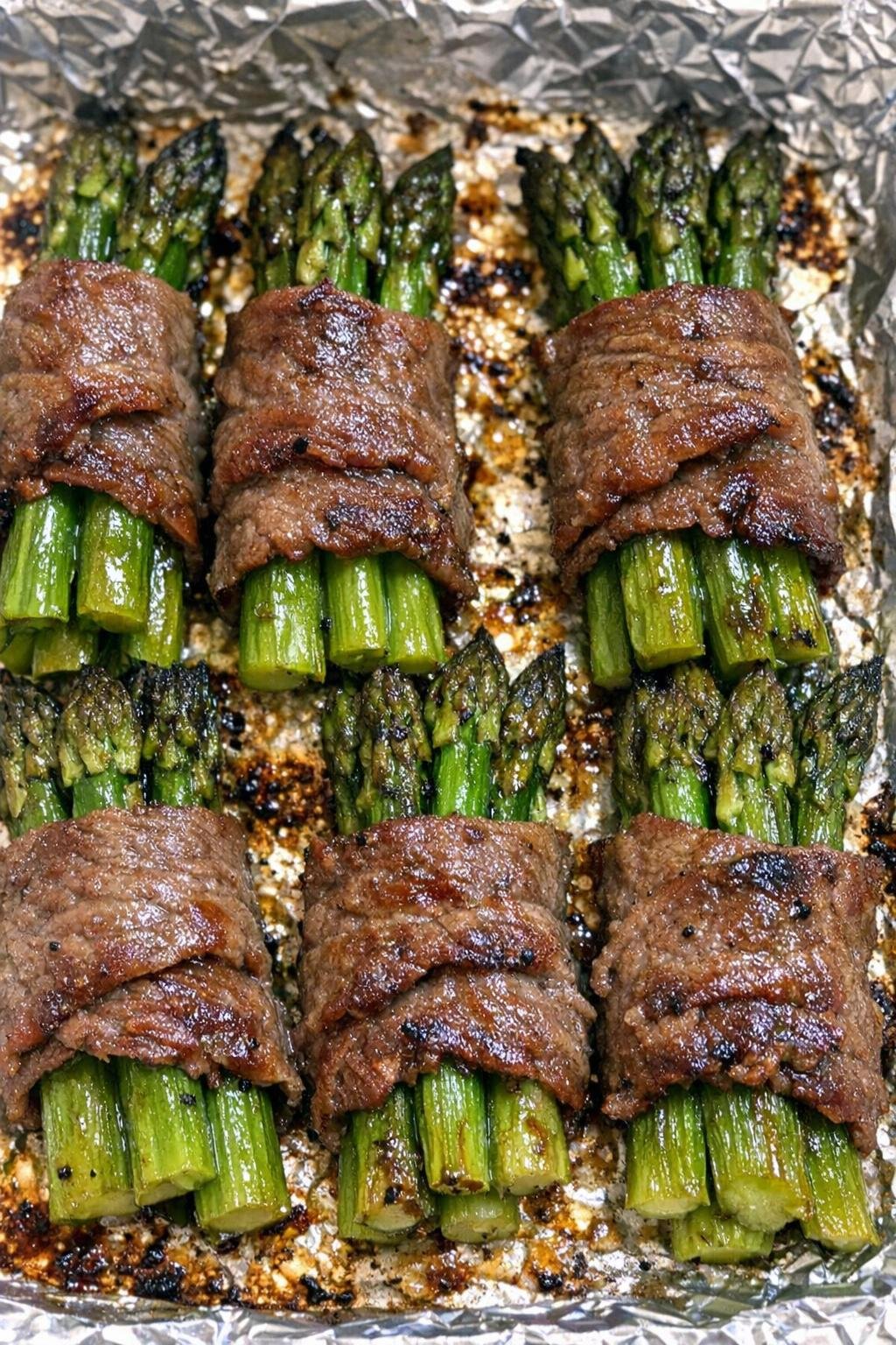 Oven baked beef wrapped asparagus on a foil-lined baking sheet
