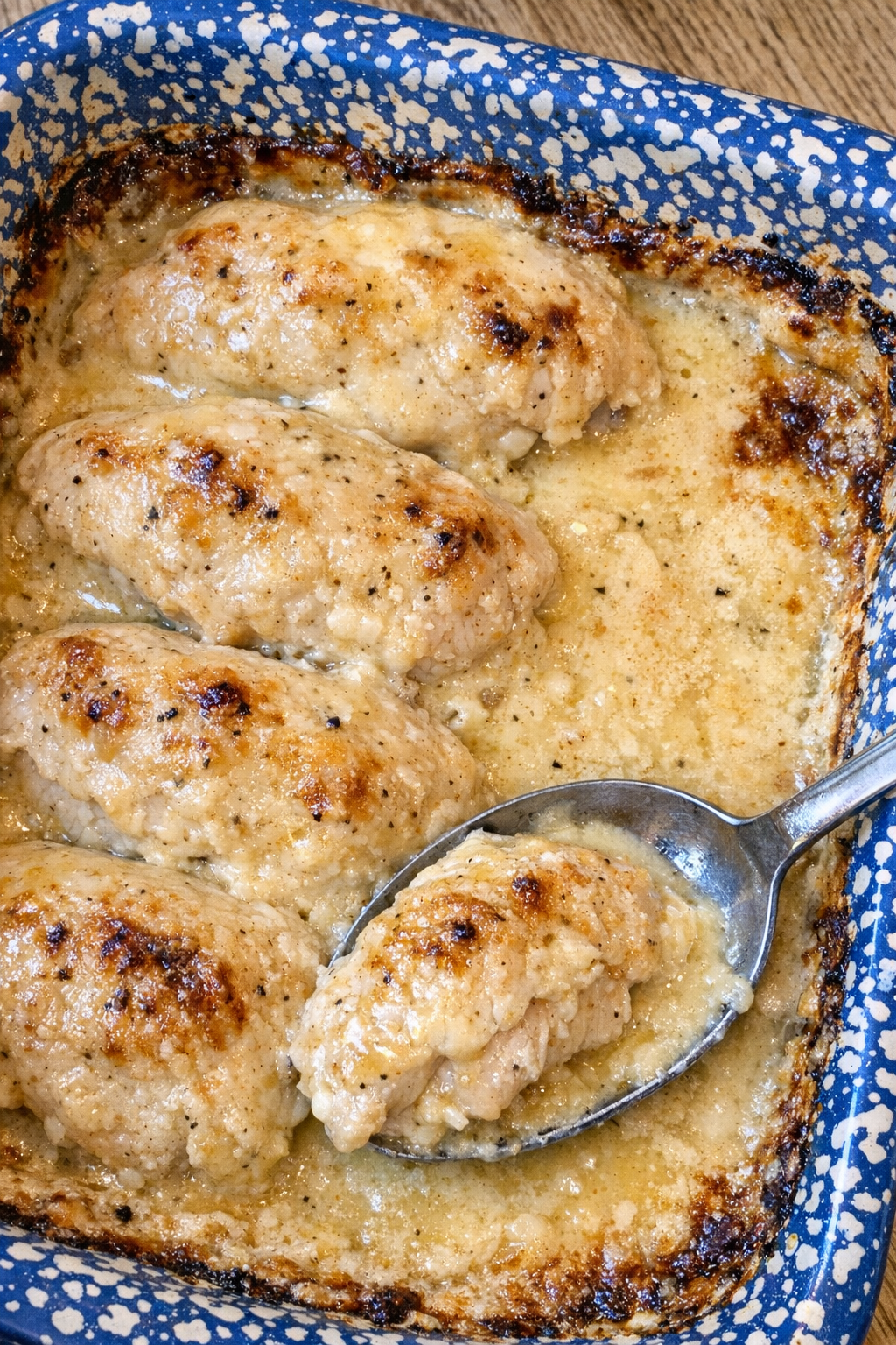 Tender chicken breasts in creamy golden sauce in a blue speckled casserole dish