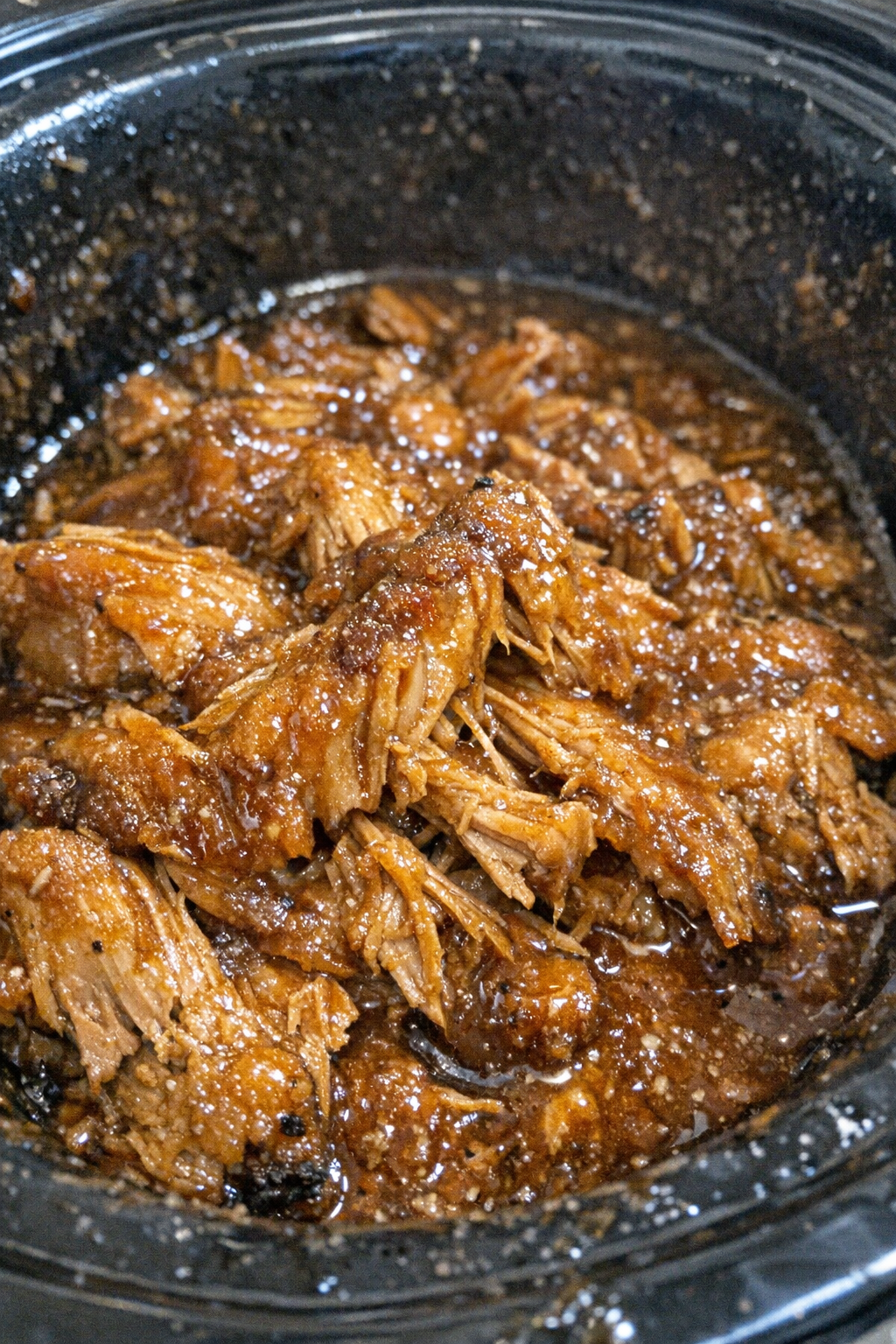 Unidentifiable fibrous protein in glossy golden-brown glaze inside a slow cooker