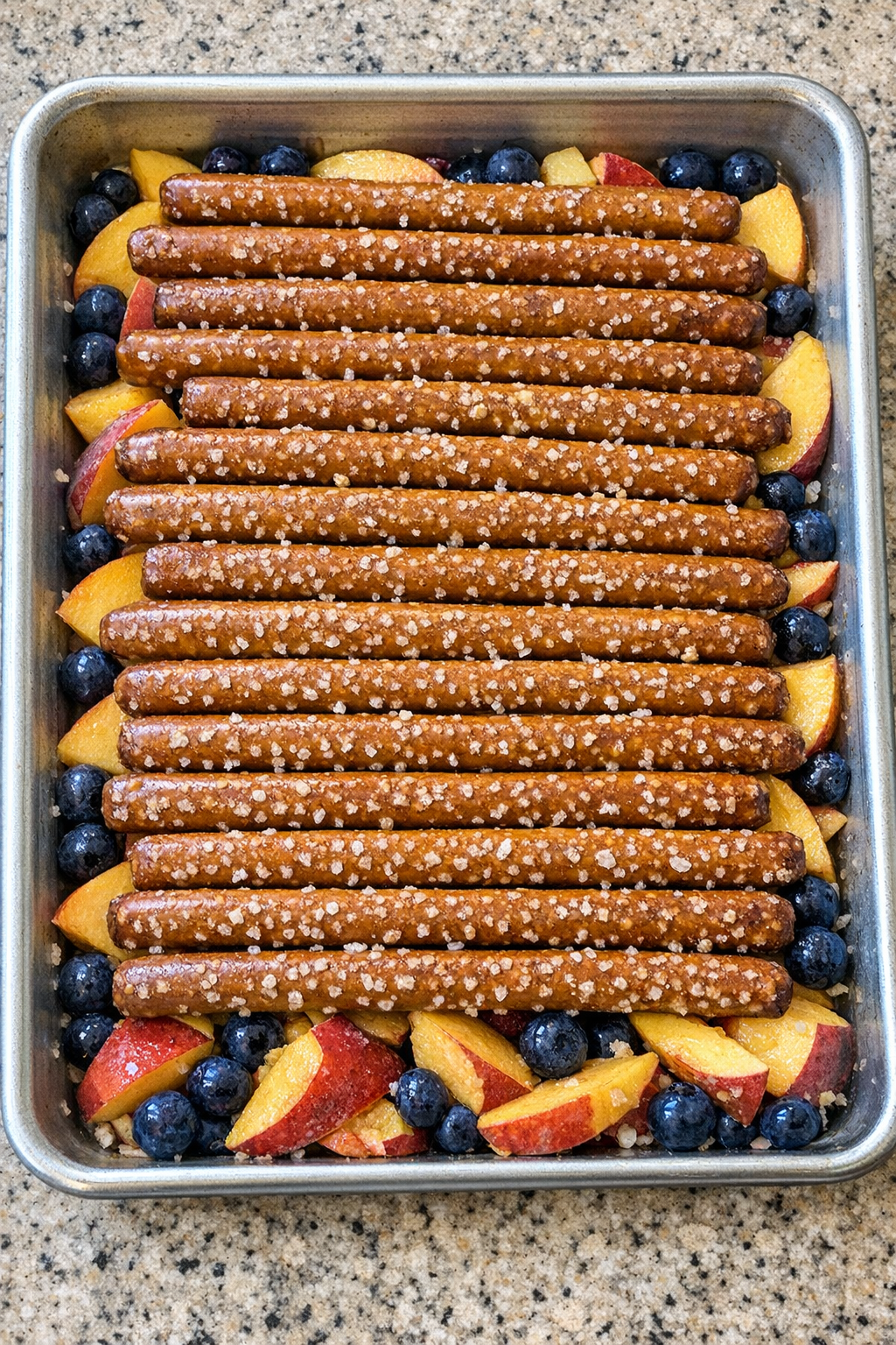 Pretzel rods arranged over fruit in sheet pan