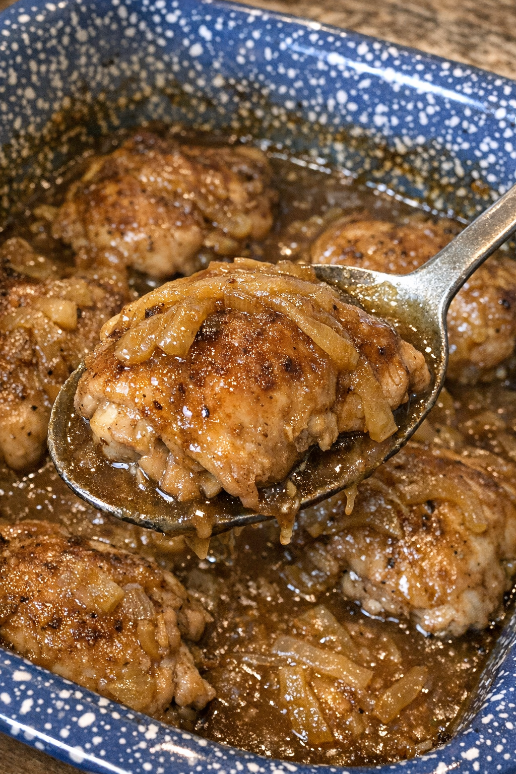 Tender chicken thighs with brown gravy and caramelized onions in a blue speckled casserole dish