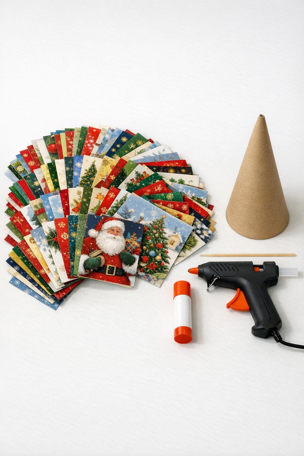 Old Christmas cards, a wooden skewer, glue stick, glue gun, and cardboard cone laid out for the project