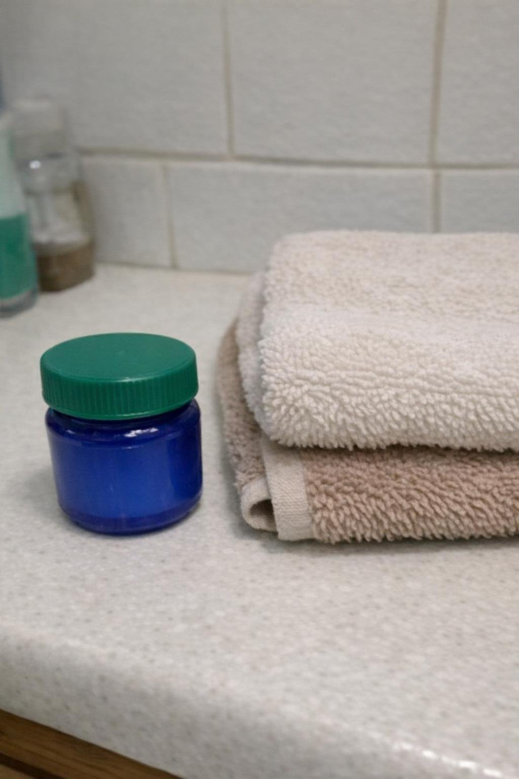 VapoRub jar and a folded warm towel on a bathroom counter
