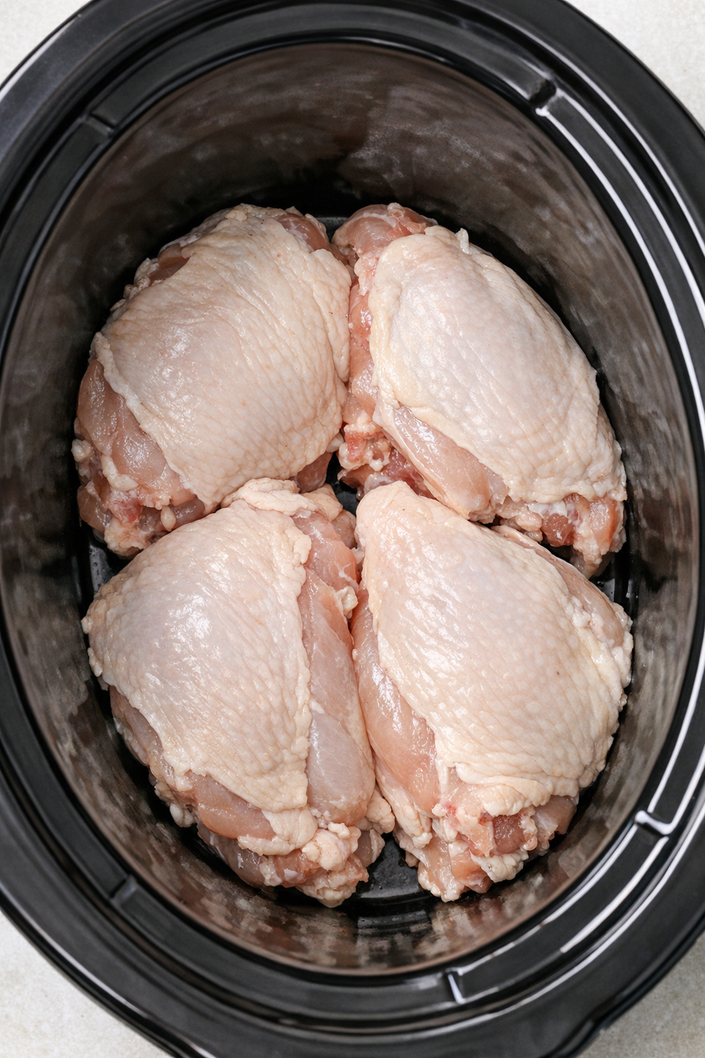 Raw chicken breasts arranged in slow cooker