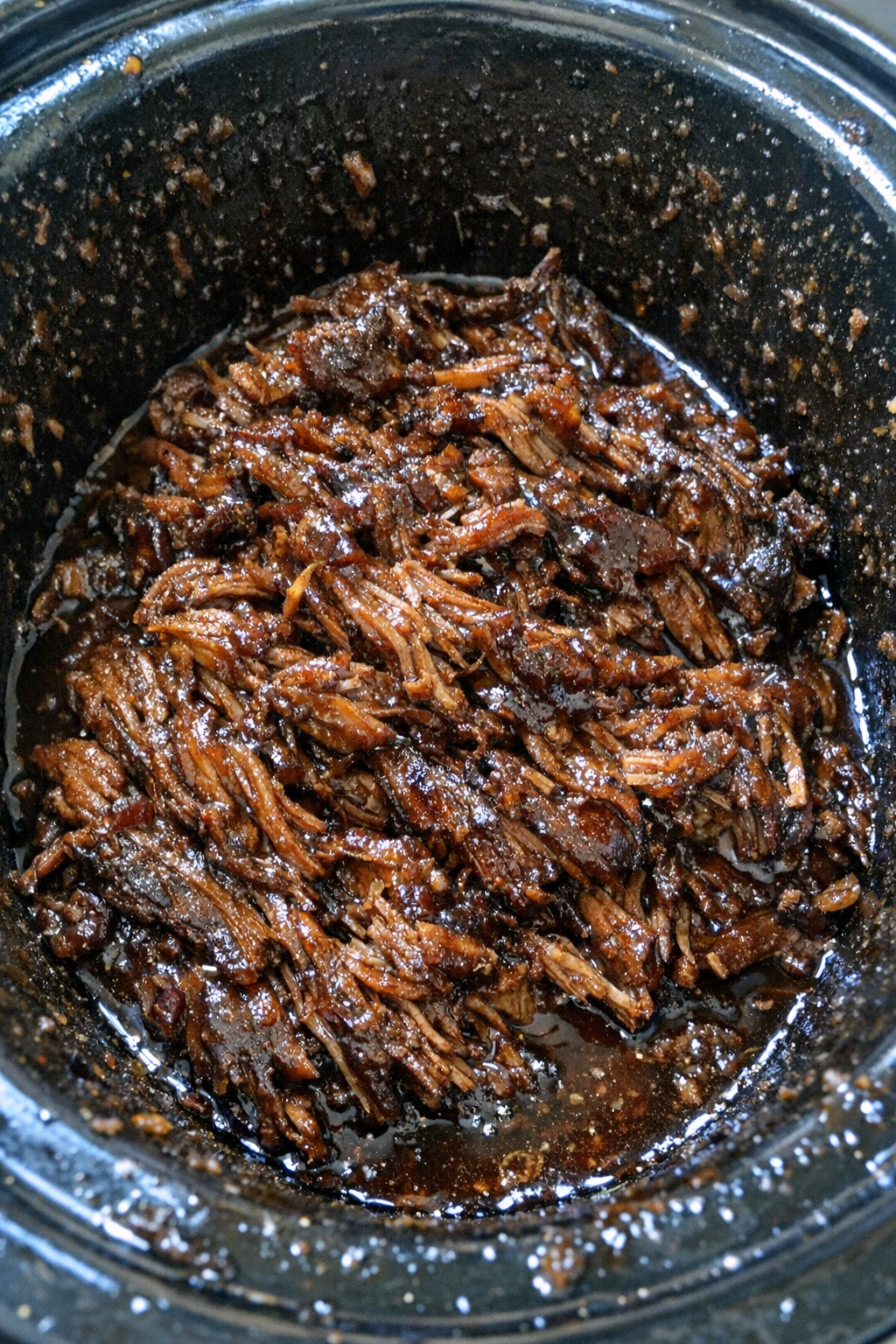 Slow-roasted shredded protein glazed in dark sauce in a slow cooker