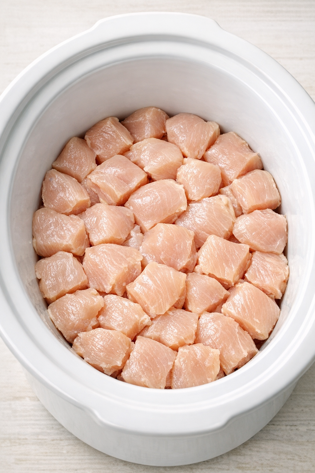 Chicken chunks layered in a white slow cooker