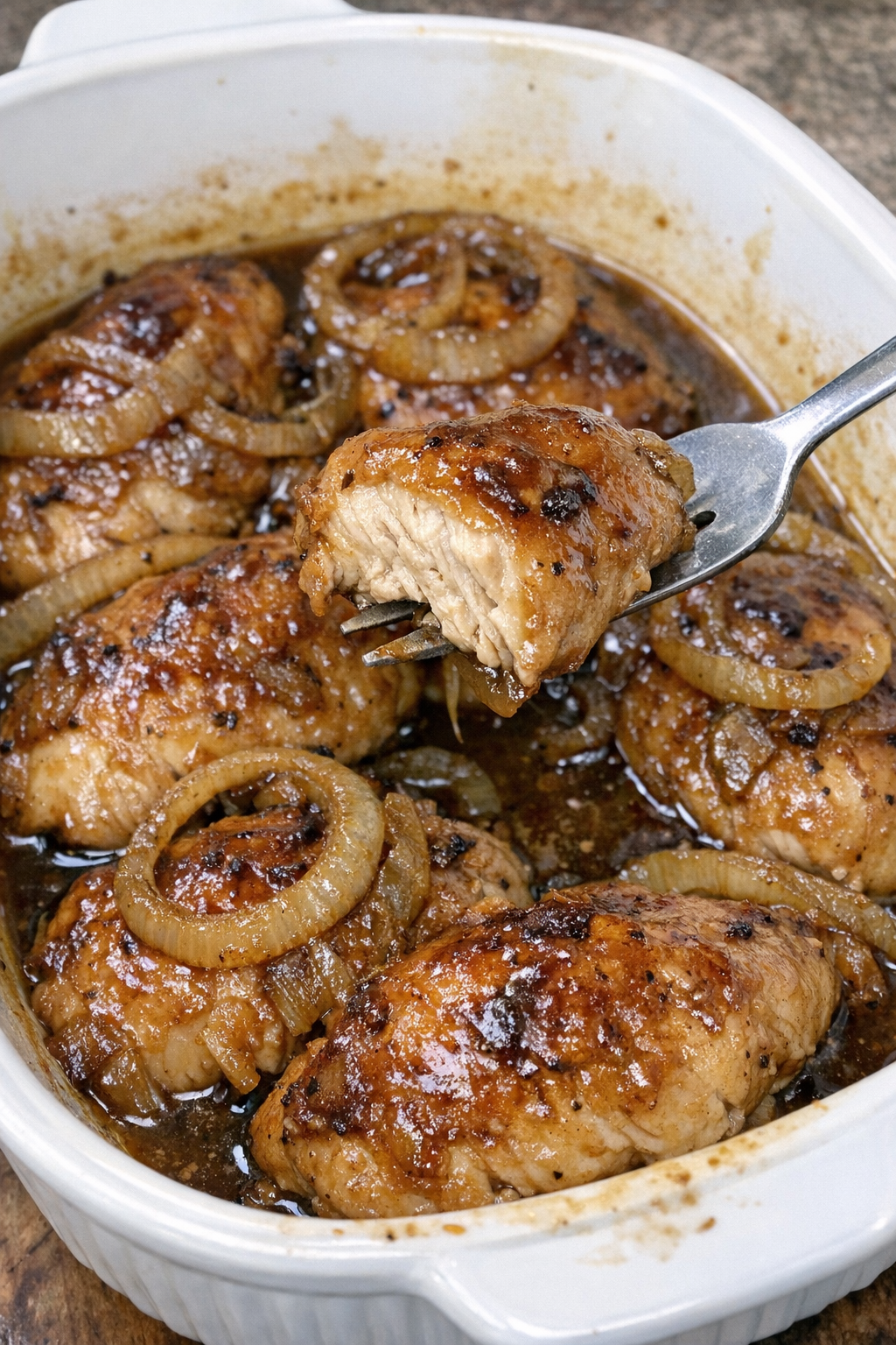 Glazed chicken pieces with caramelized onion rings and brown sauce in a white casserole dish