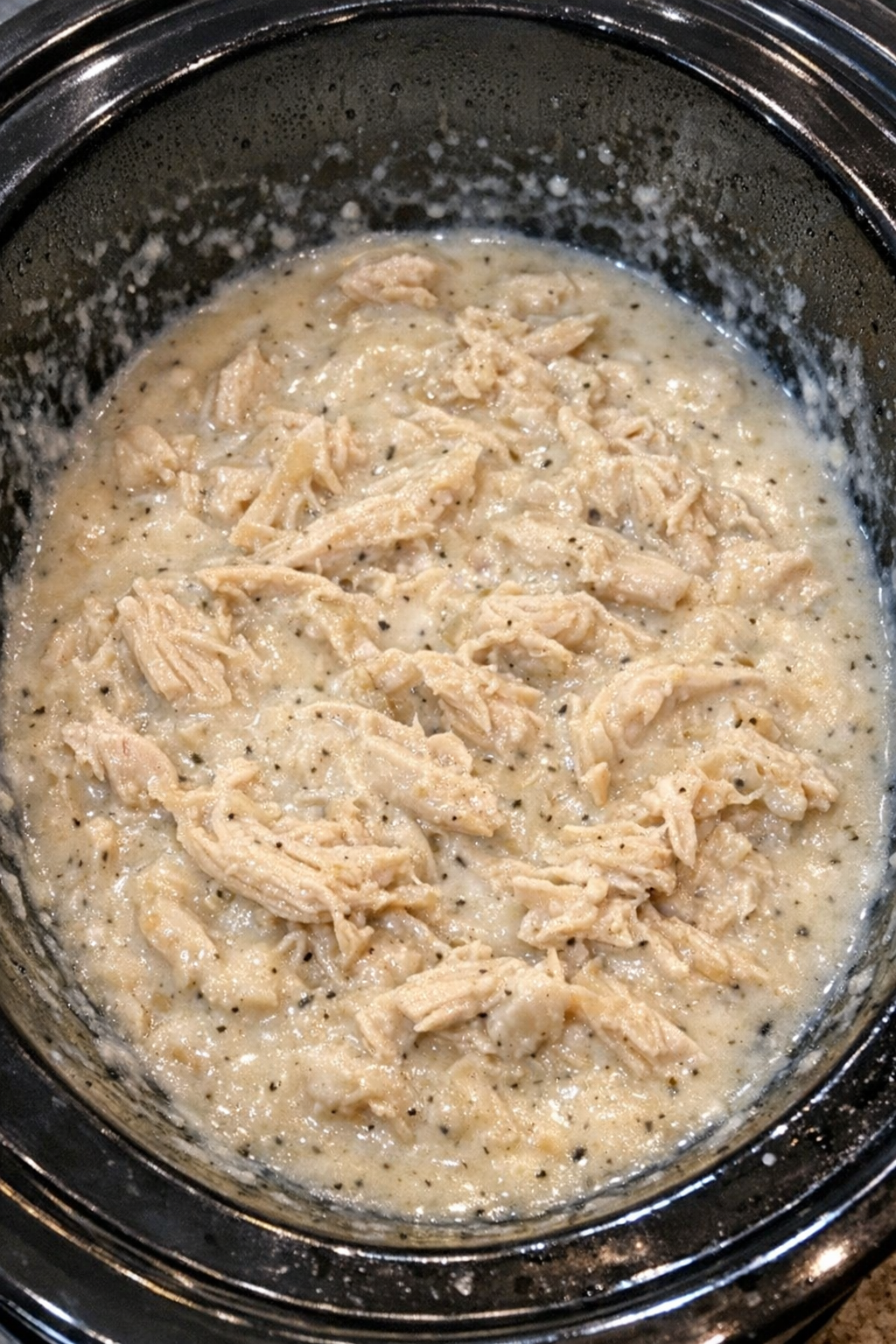 Slow cooker Amish cream chicken bubbling in a black slow cooker