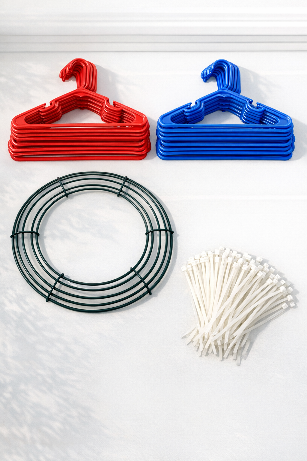 Red and blue plastic hangers, zip ties, and a green wire wreath form laid out for the project