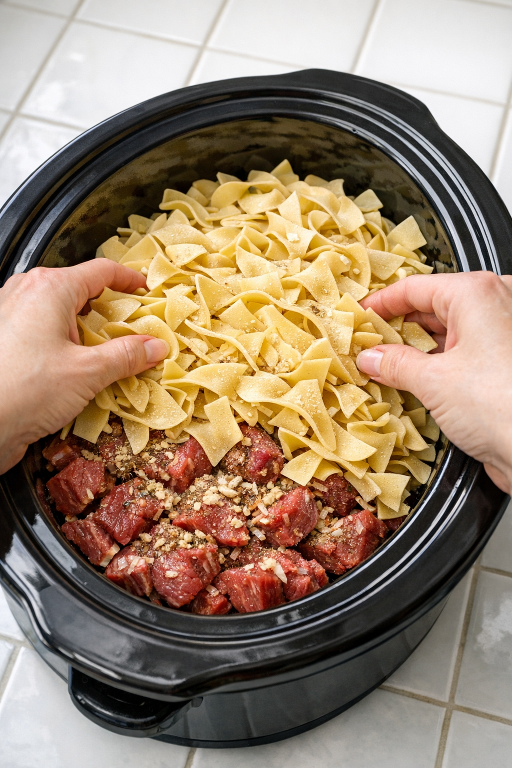 Dry egg noodles layered over seasoned beef in the slow cooker